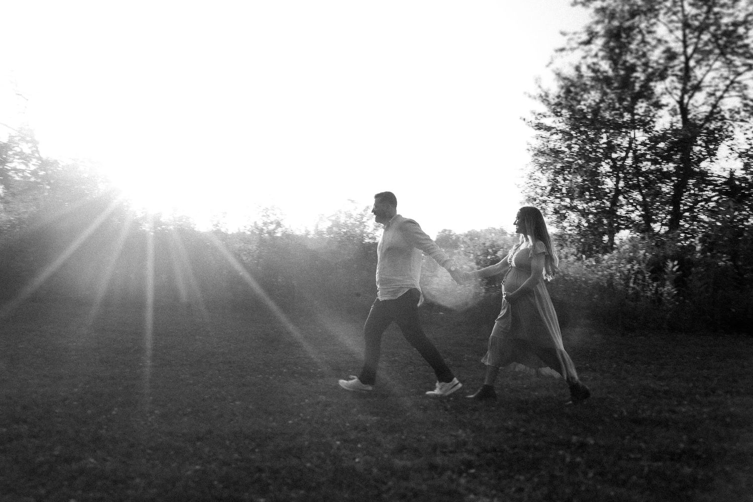 Silhouetted figures embrace on a hilltop during golden hour with sun flares in background.