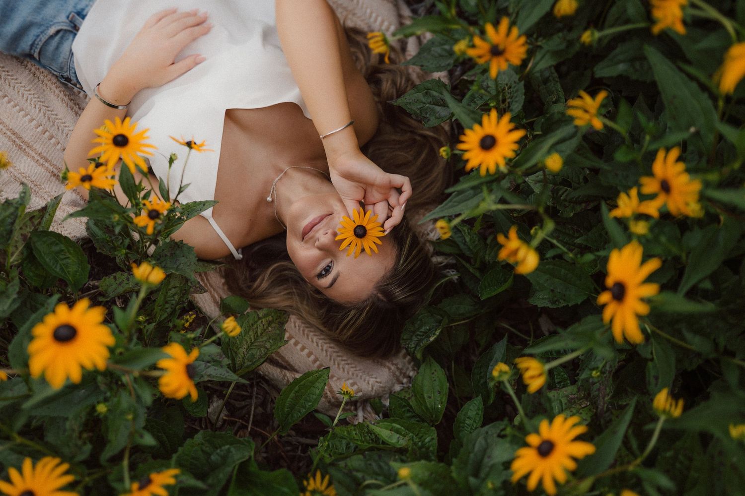 Someone lying down in a garden surrounded by vibrant yellow flowers and green foliage from above perspective.