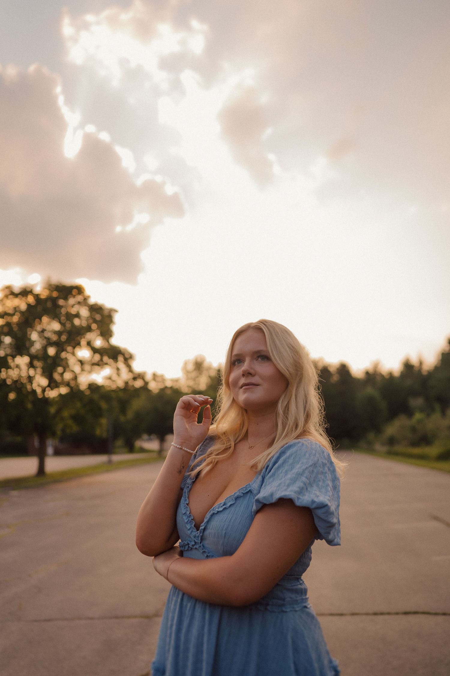 Person in blue dress gazing at sunset sky in golden hour lighting.