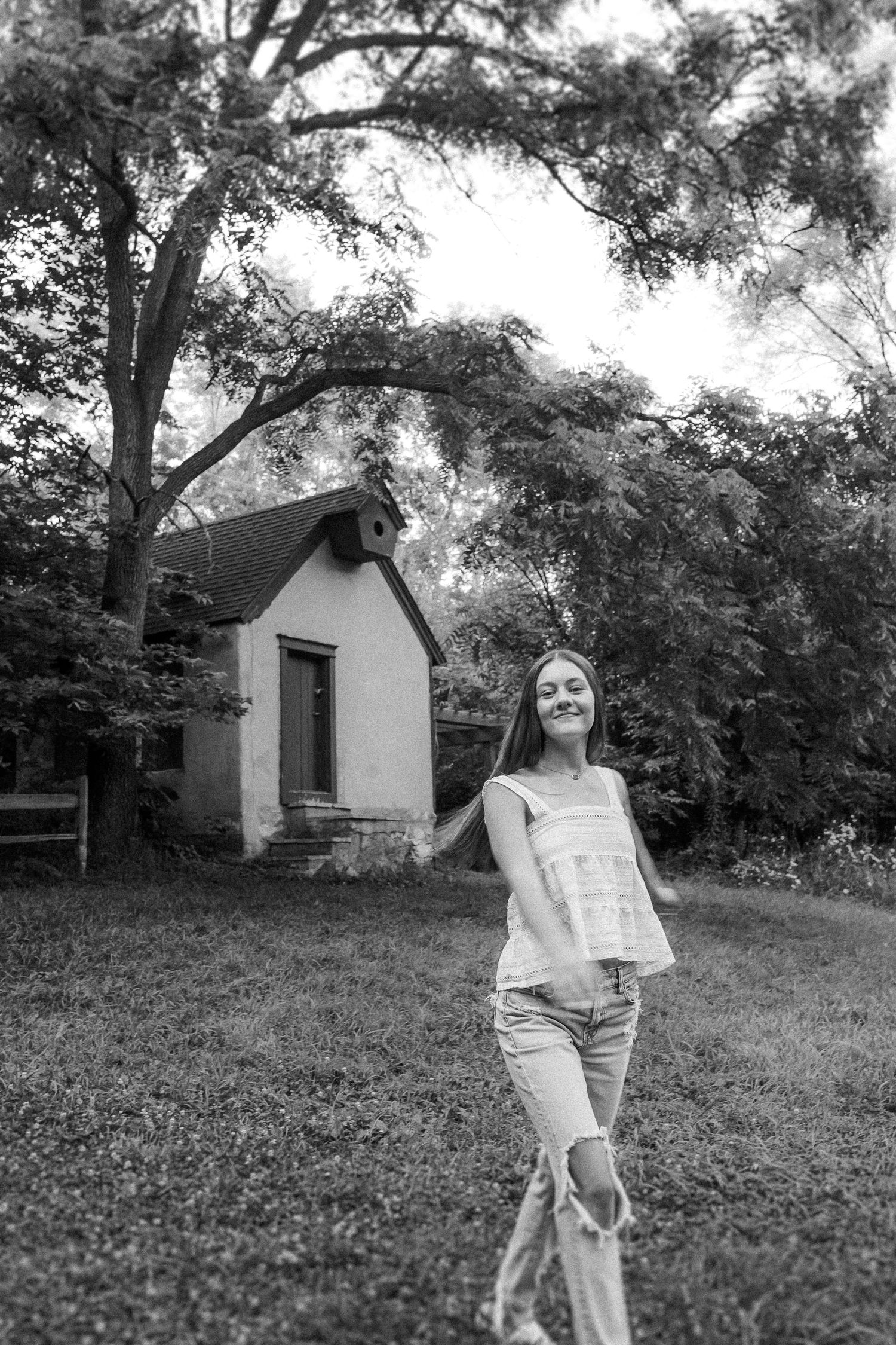 Black and white photo showing a small white cottage surrounded by trees on a grassy hill.