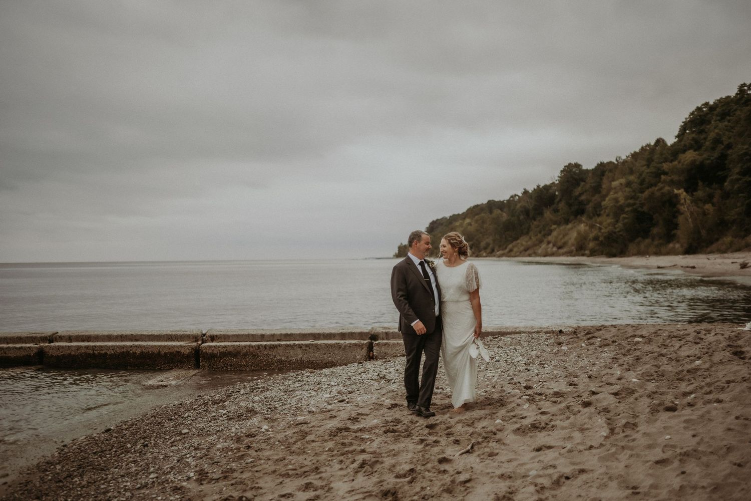 Newlyweds standing together on misty beach with cliffs in background.