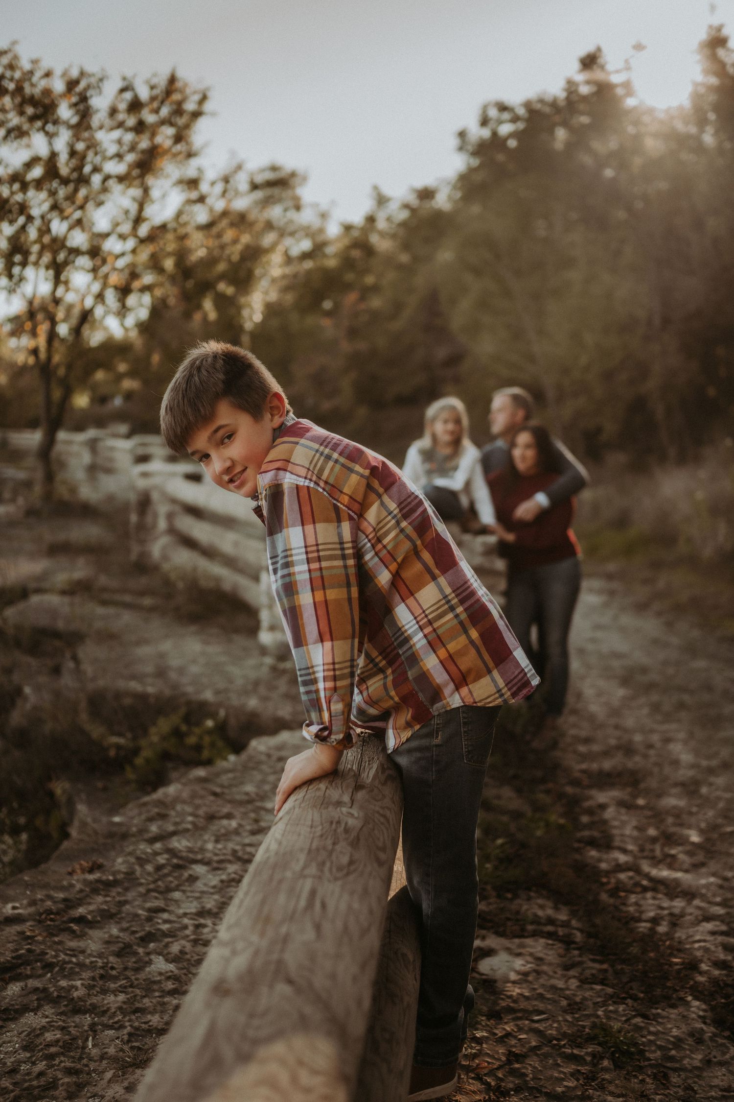 Child plays on wooden fence post while others watch in background during sunset nature walk.