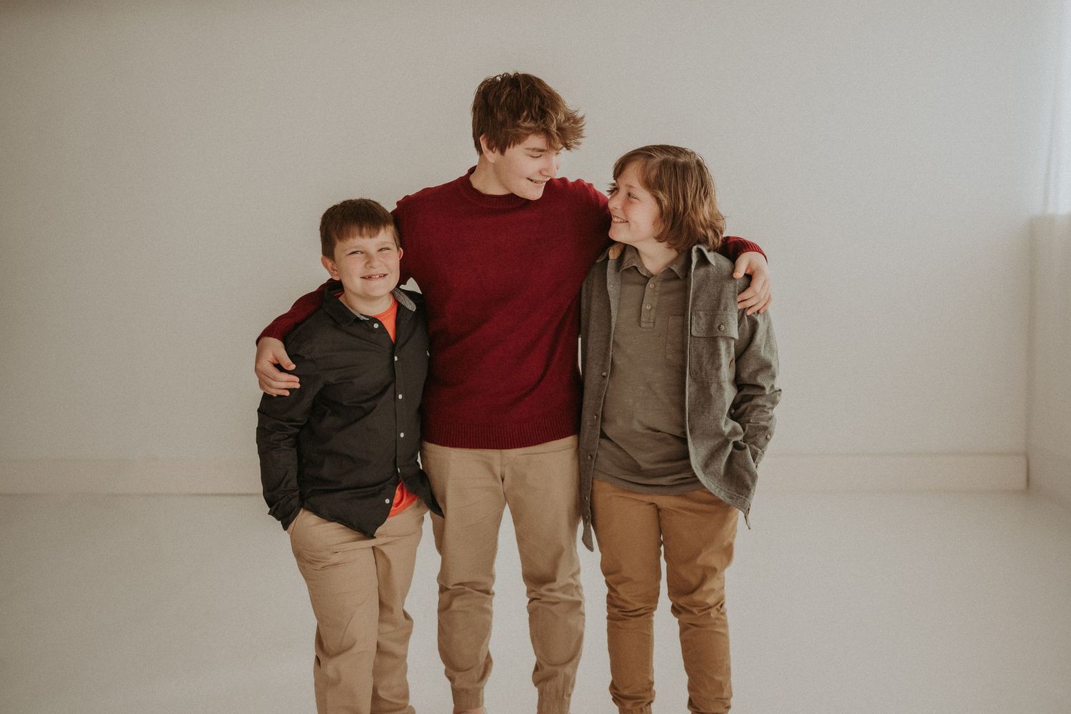 Three young people in casual clothes share warm moment against white studio background.