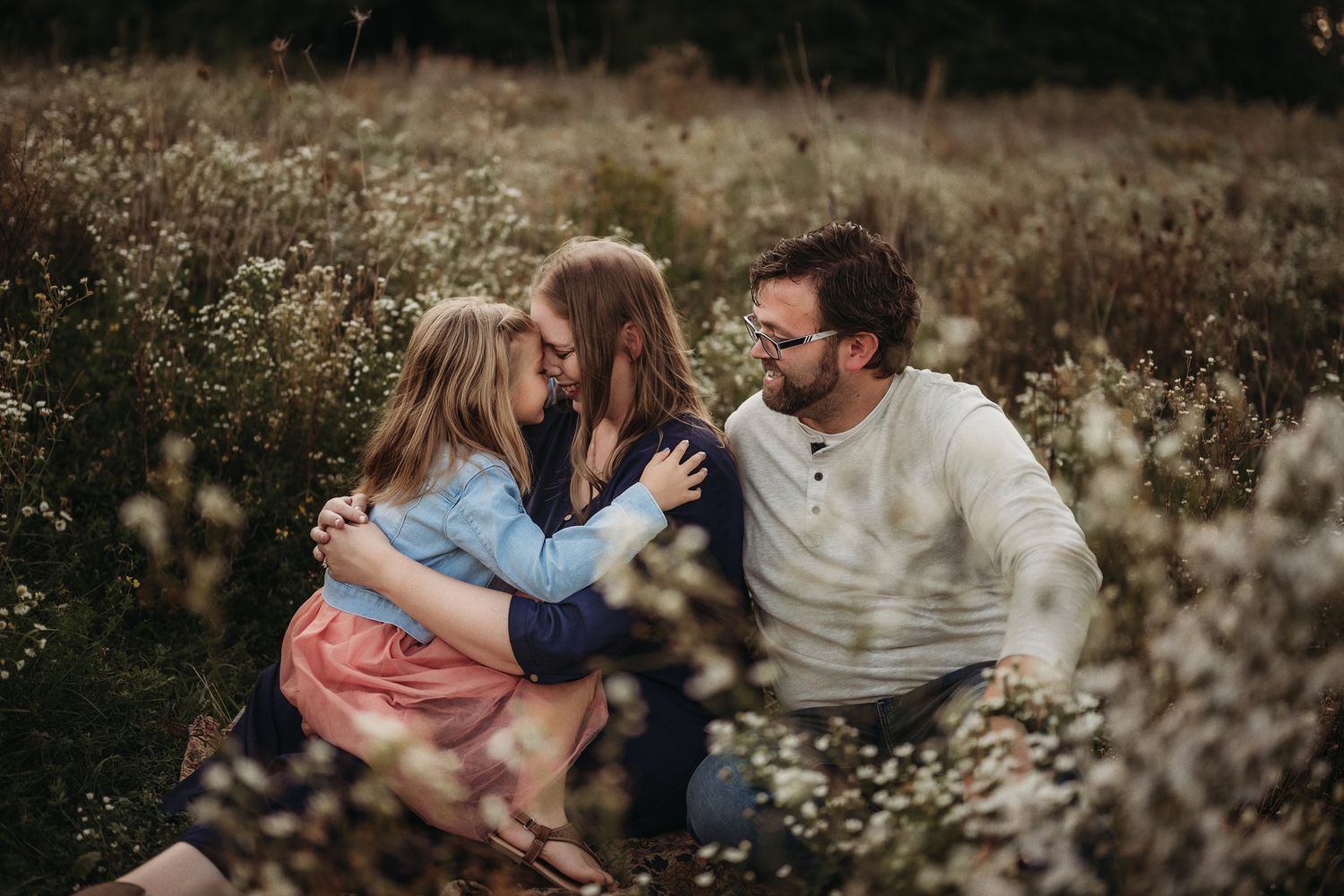 Family sharing tender moments together in a field of white flowers.