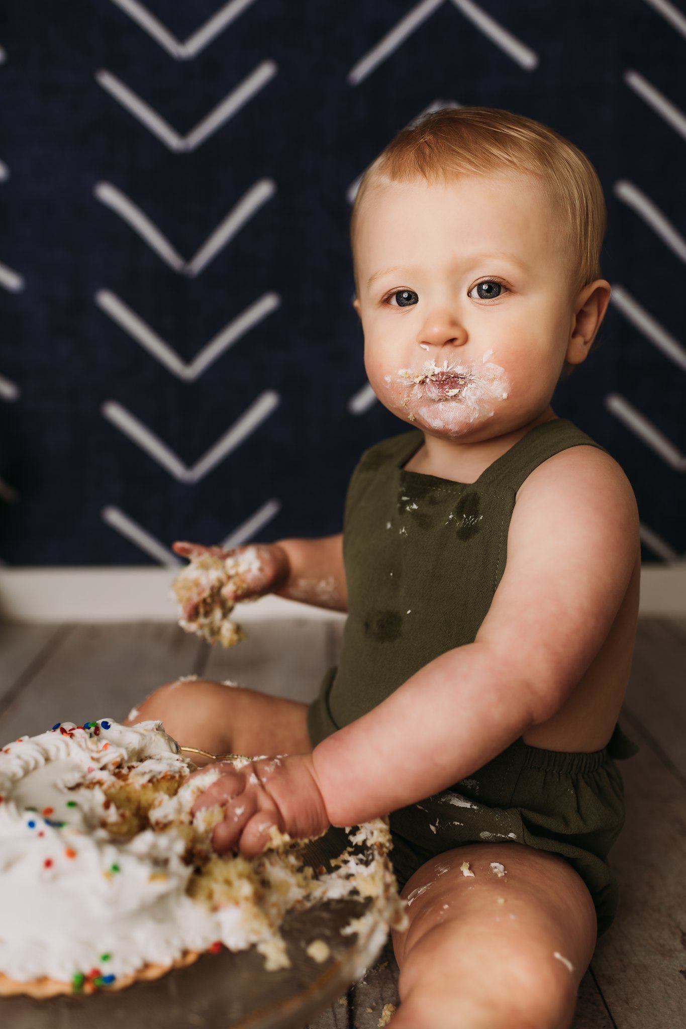 A messy cake smash scene showing frosting and sprinkles scattered on a glass cake stand.