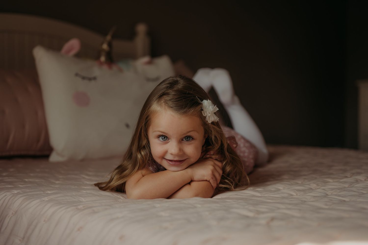 Indoor portrait of child lying on bed with decorative pillows in background.