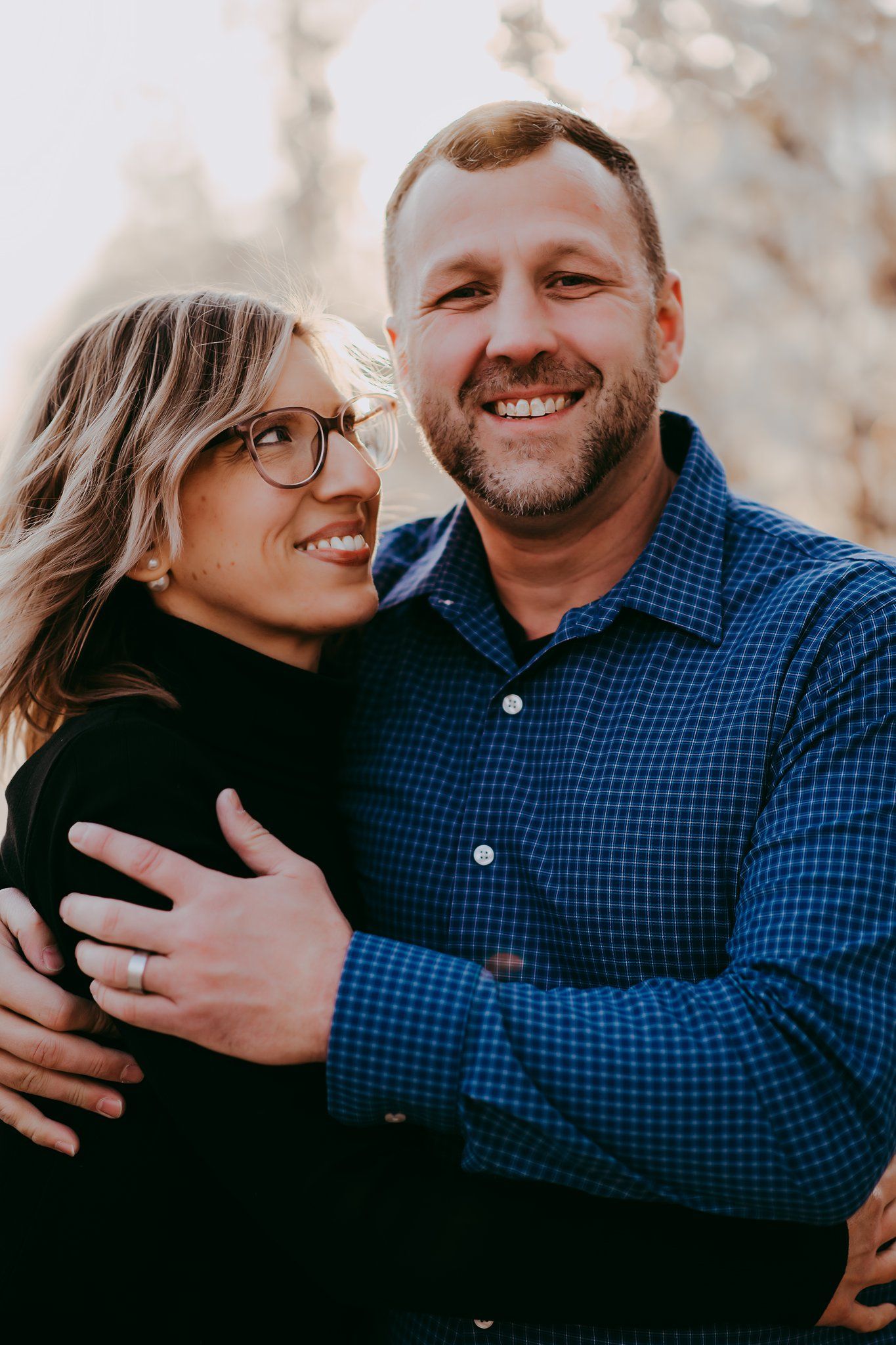 Loving couple embraces outdoors in casual attire during golden hour photoshoot.