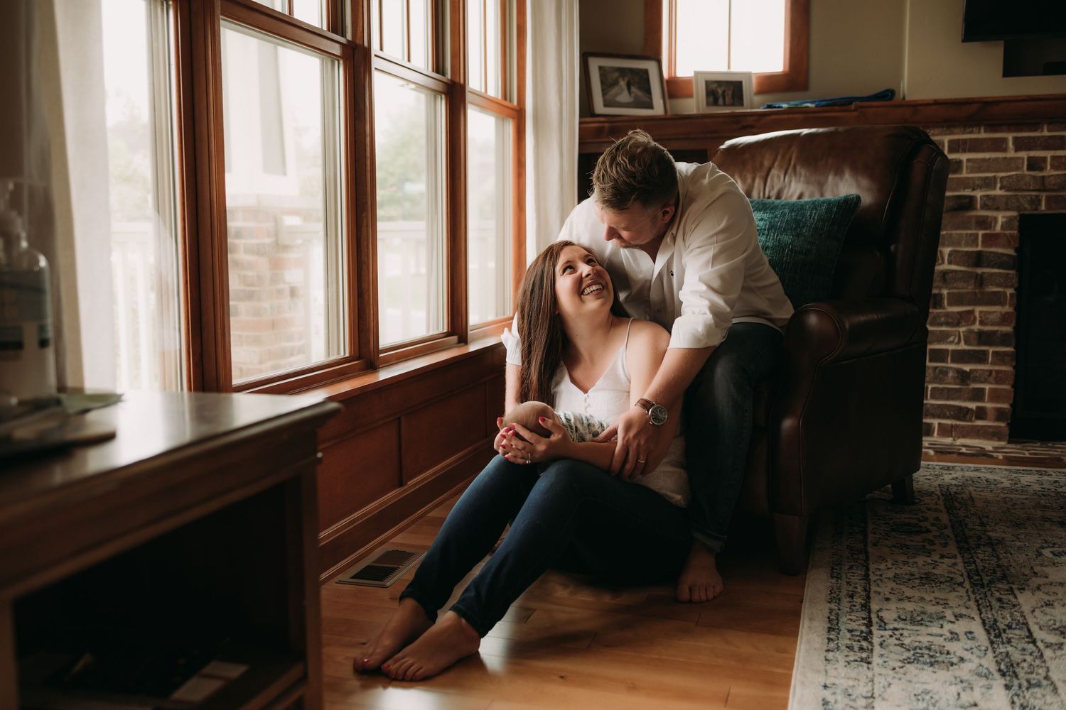 A couple shares an intimate moment near bright windows in a cozy room with wooden floors.