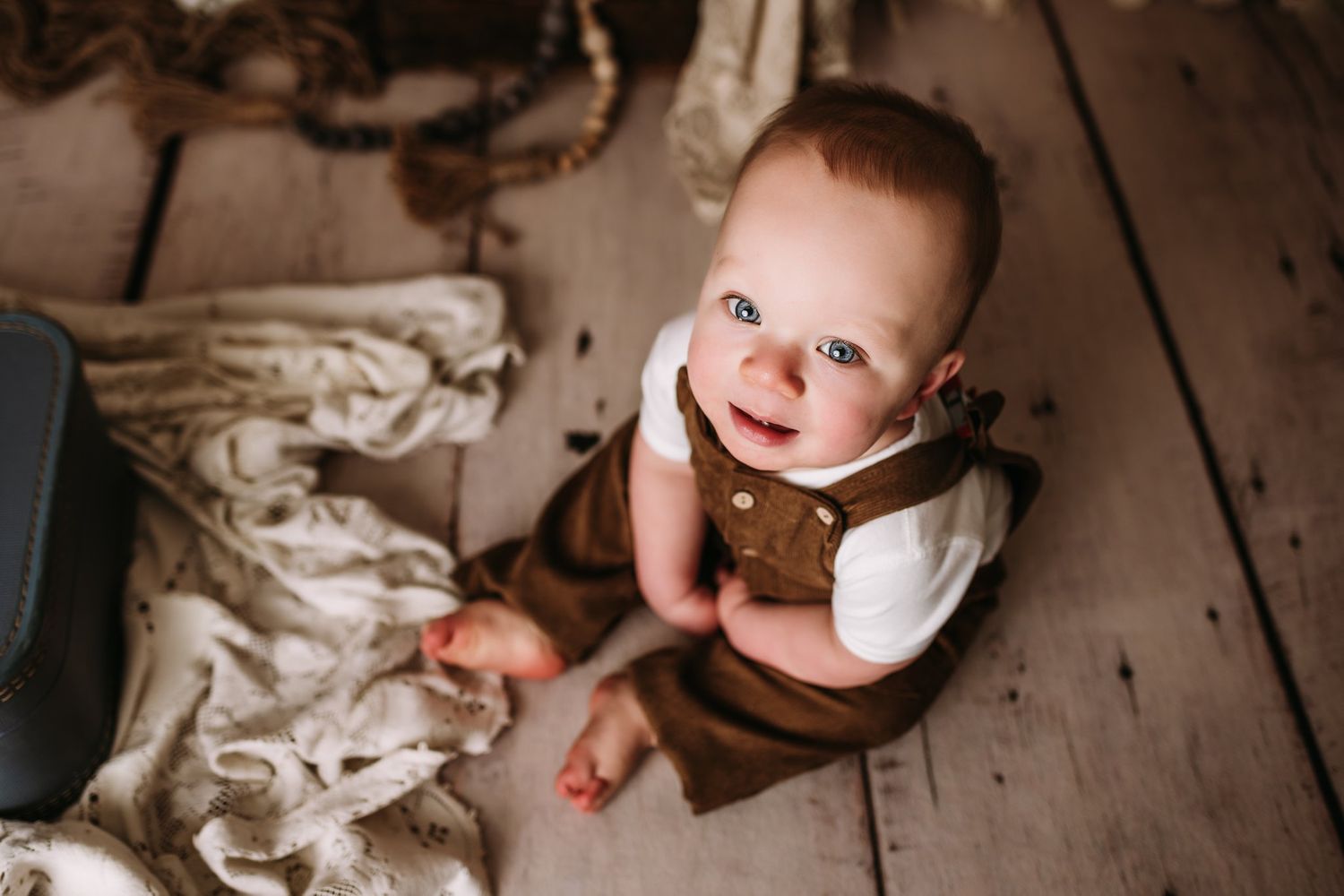 Looking up view of brown overalls on wooden floor with cream fabric background.