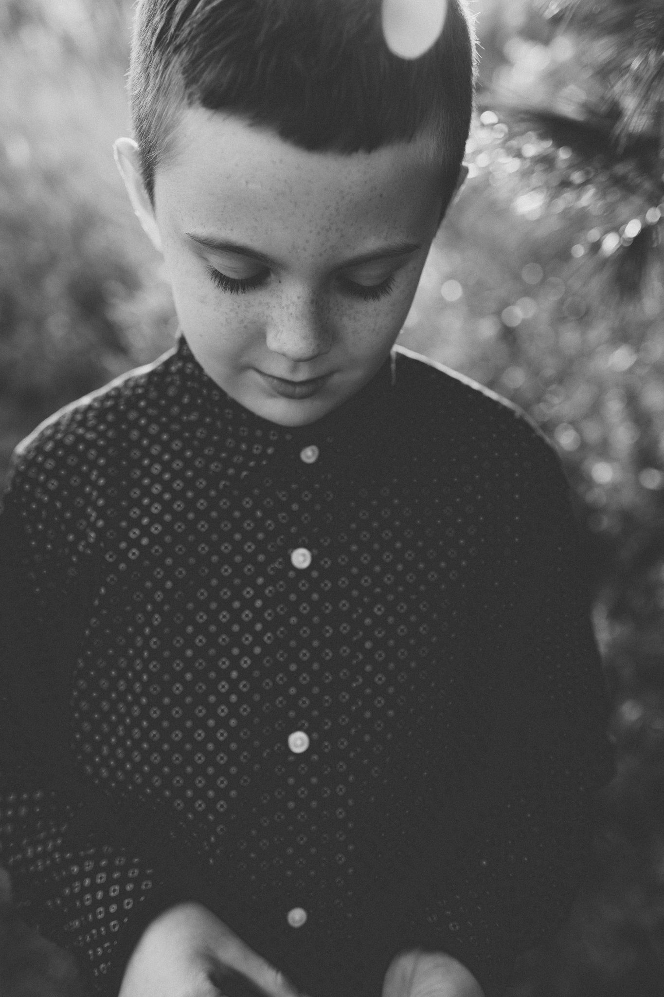 Black and white portrait of a young child in a polka dot button-up shirt looking down.