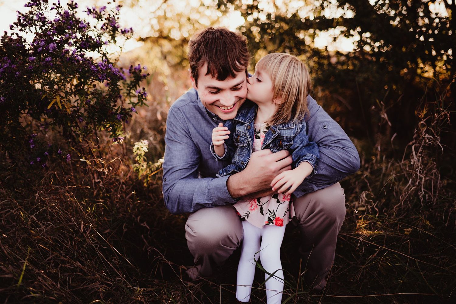 Two people share an intimate moment while crouching in tall grass during sunset.