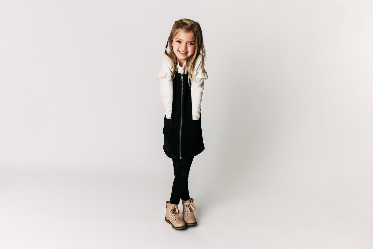 Child in black vest and white sleeves poses stylishly against white backdrop.