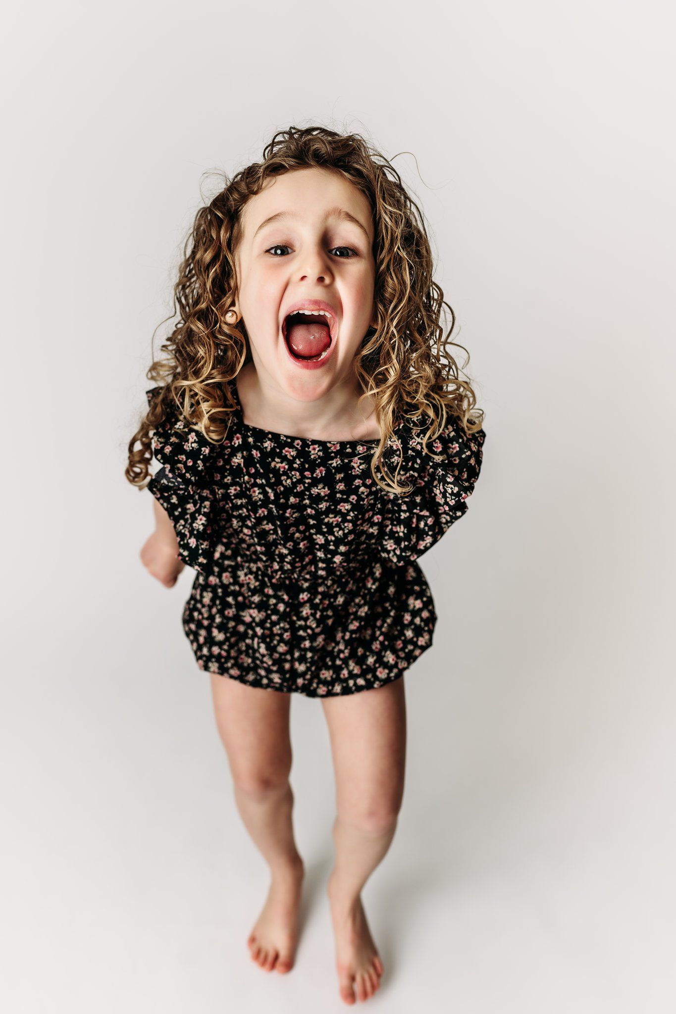 A child in a floral romper jumps with excitement against a white background.