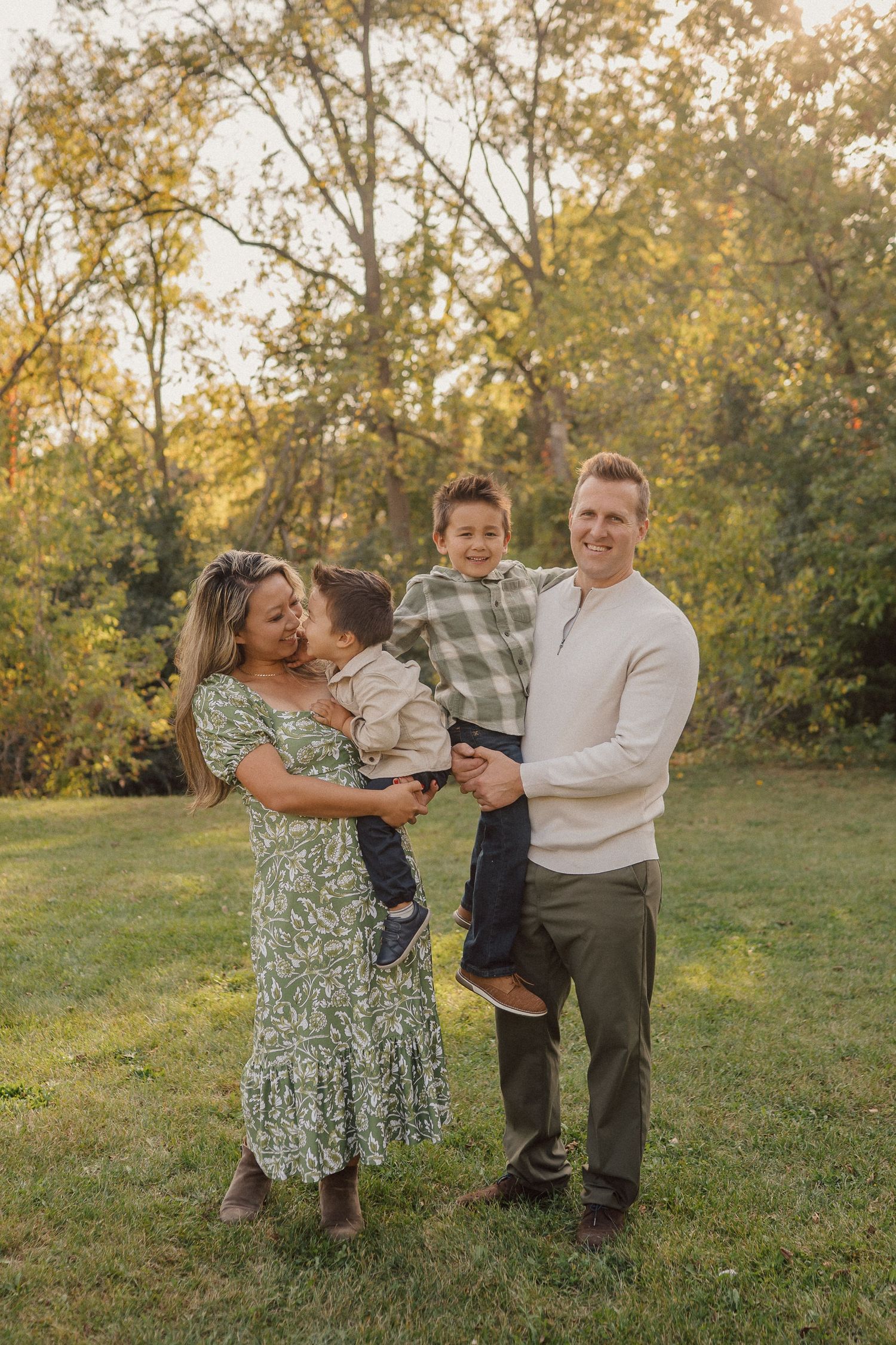 A family enjoys a warm autumn evening together outdoors with golden sunlight filtering through trees in the background.