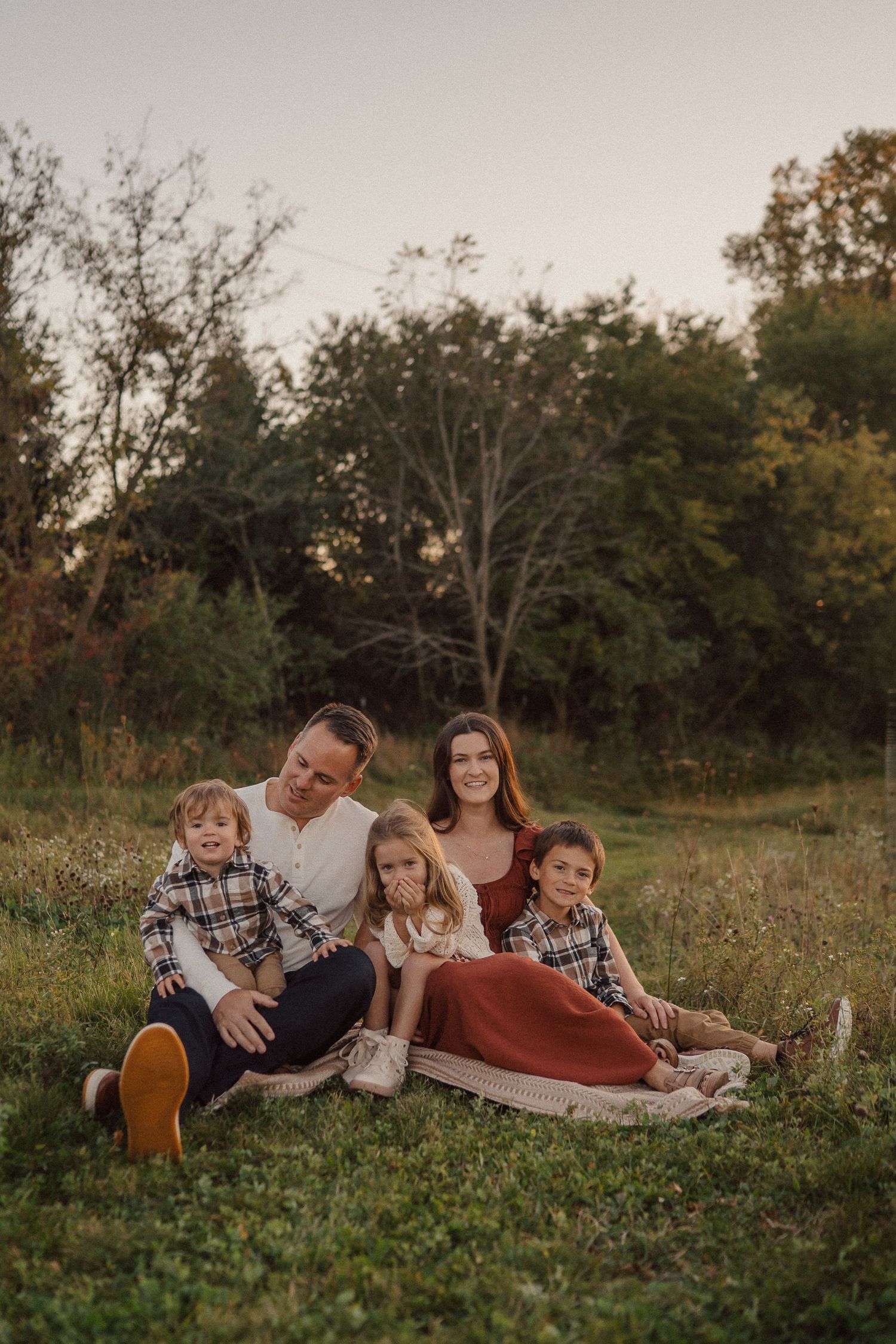 A family relaxes together on a blanket in a rustic field during a warm autumn evening.