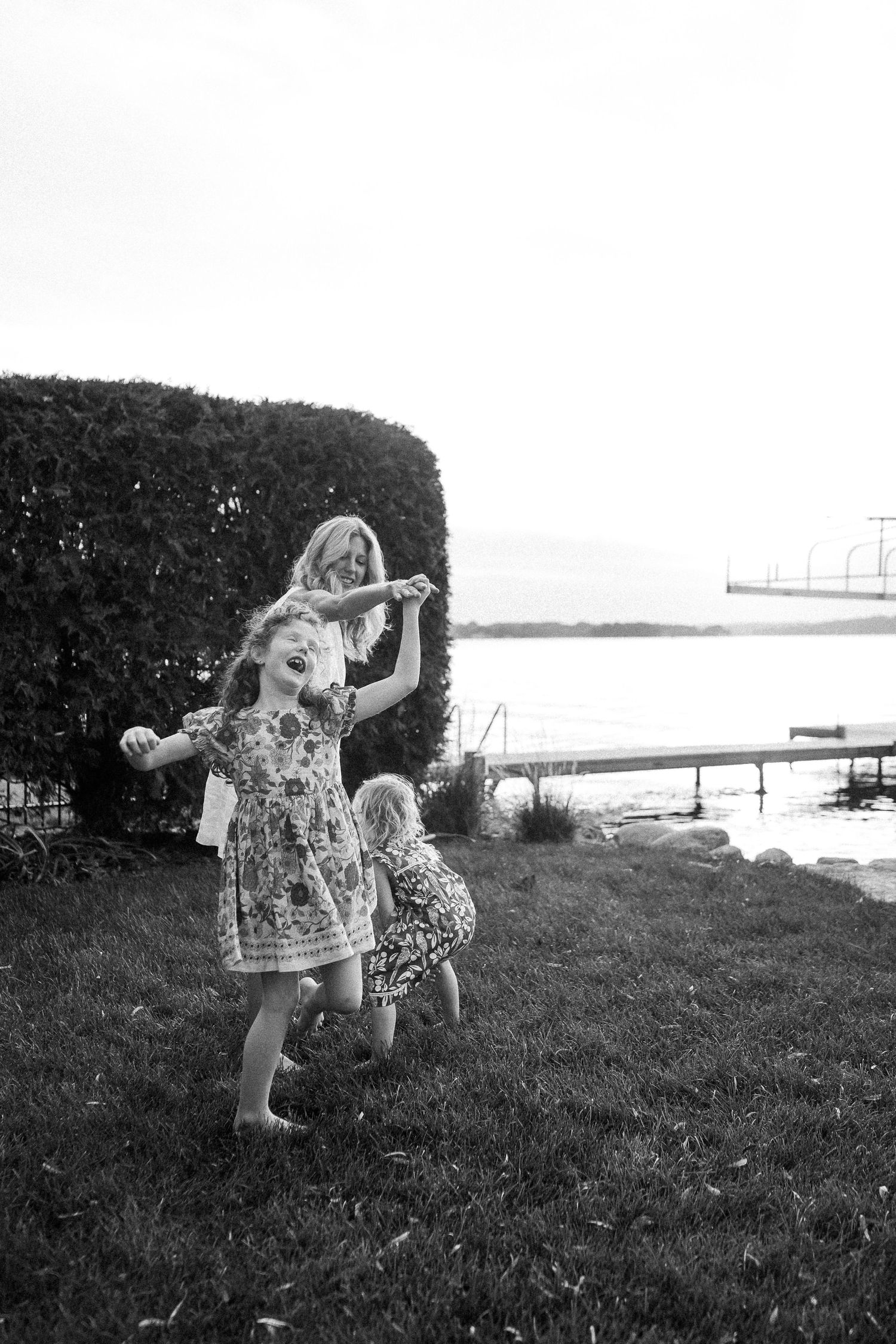 A sequence of black and white photos showing someone twirling and dancing joyfully in a floral dress on a grassy hillside.