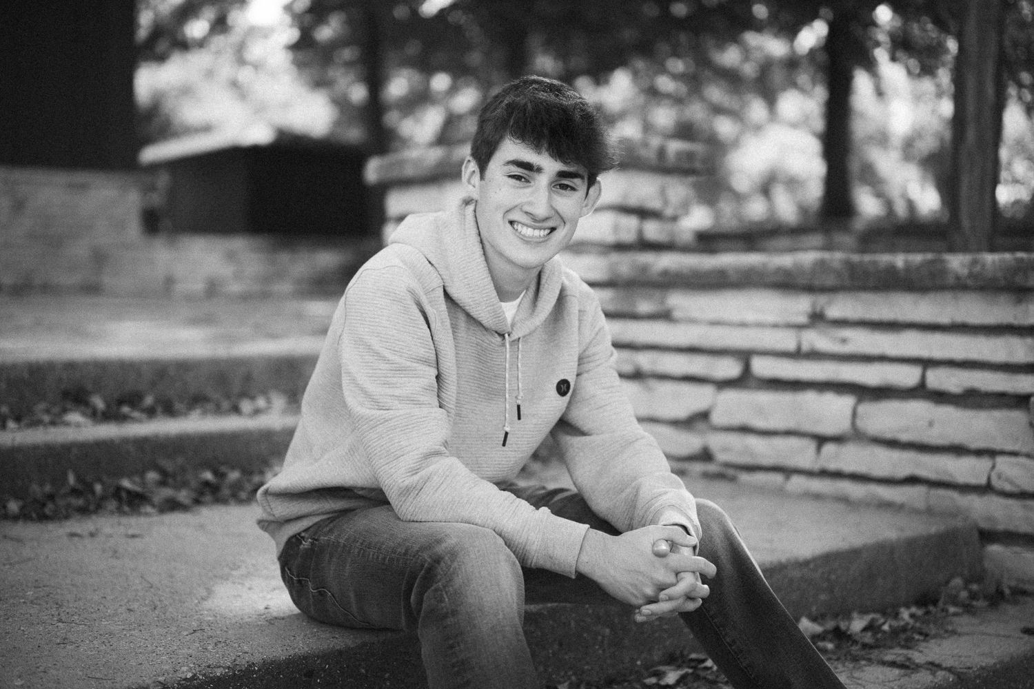 A casual portrait of someone sitting on stone steps with trees in the background.