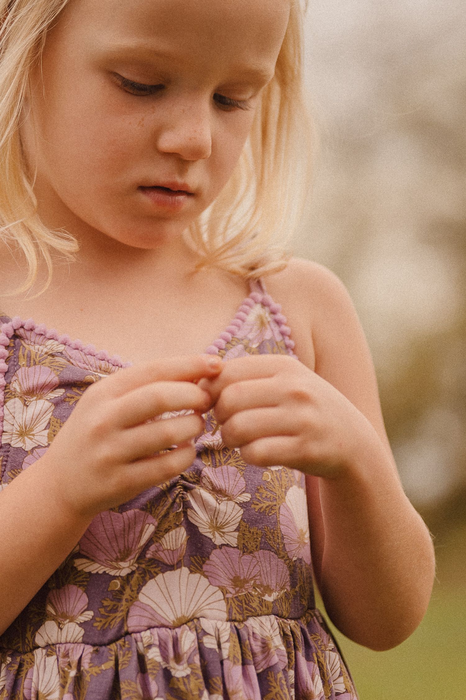 Young child in a floral dress examining details of their clothing in soft lighting.