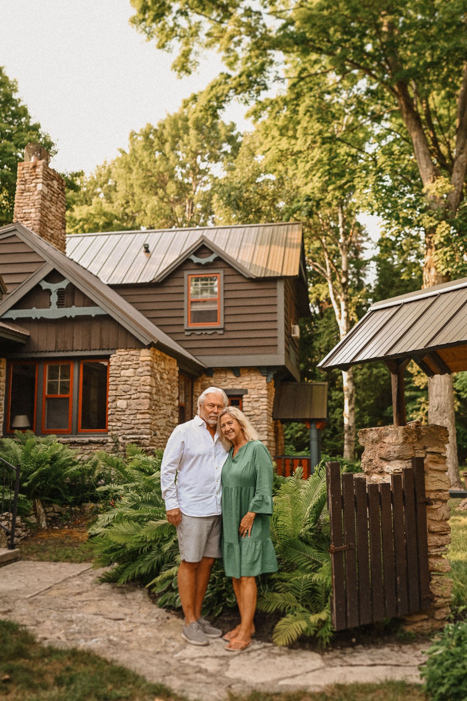 Mature couple standing together on stone path in front of rustic cottage.