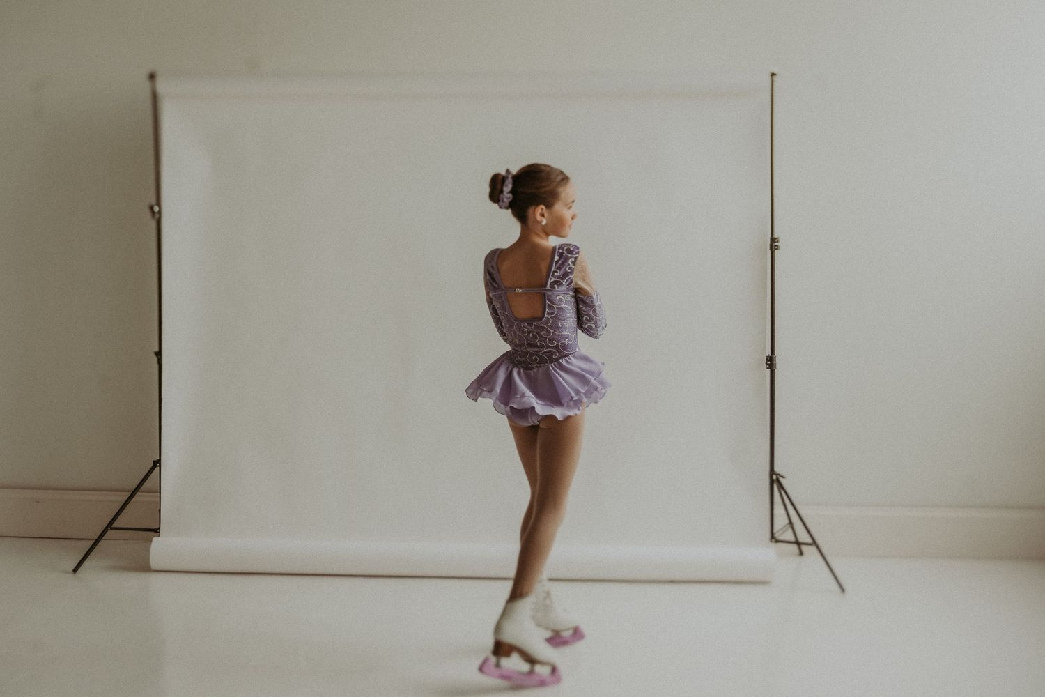Figure skater in purple dress strikes elegant pose against white backdrop.