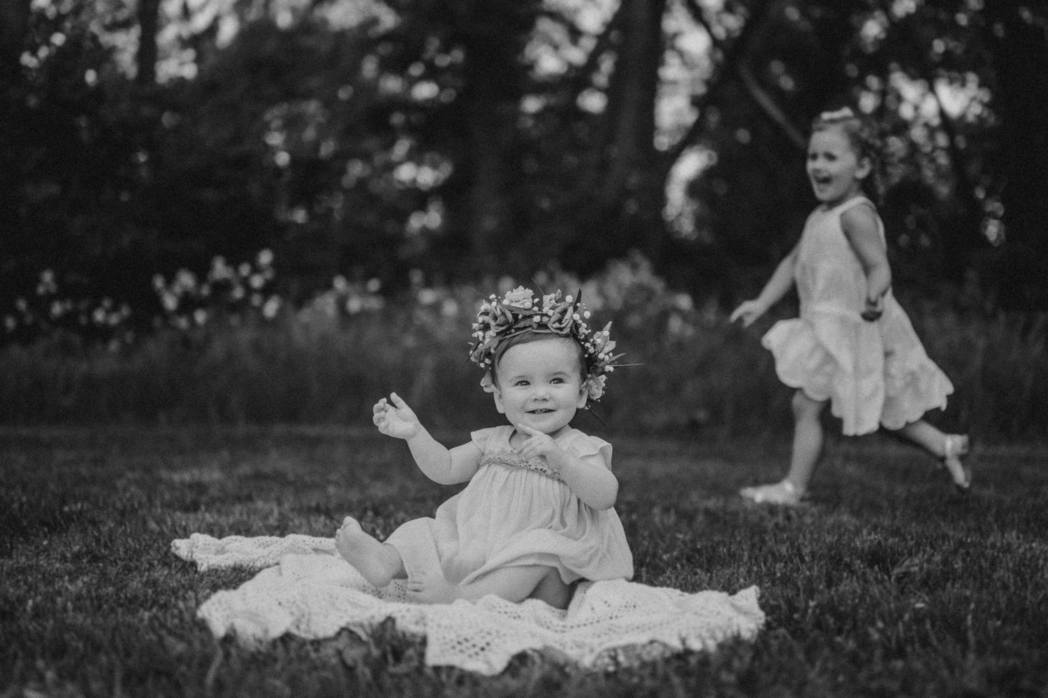 Two young children in dresses playing on a grassy lawn in black and white.