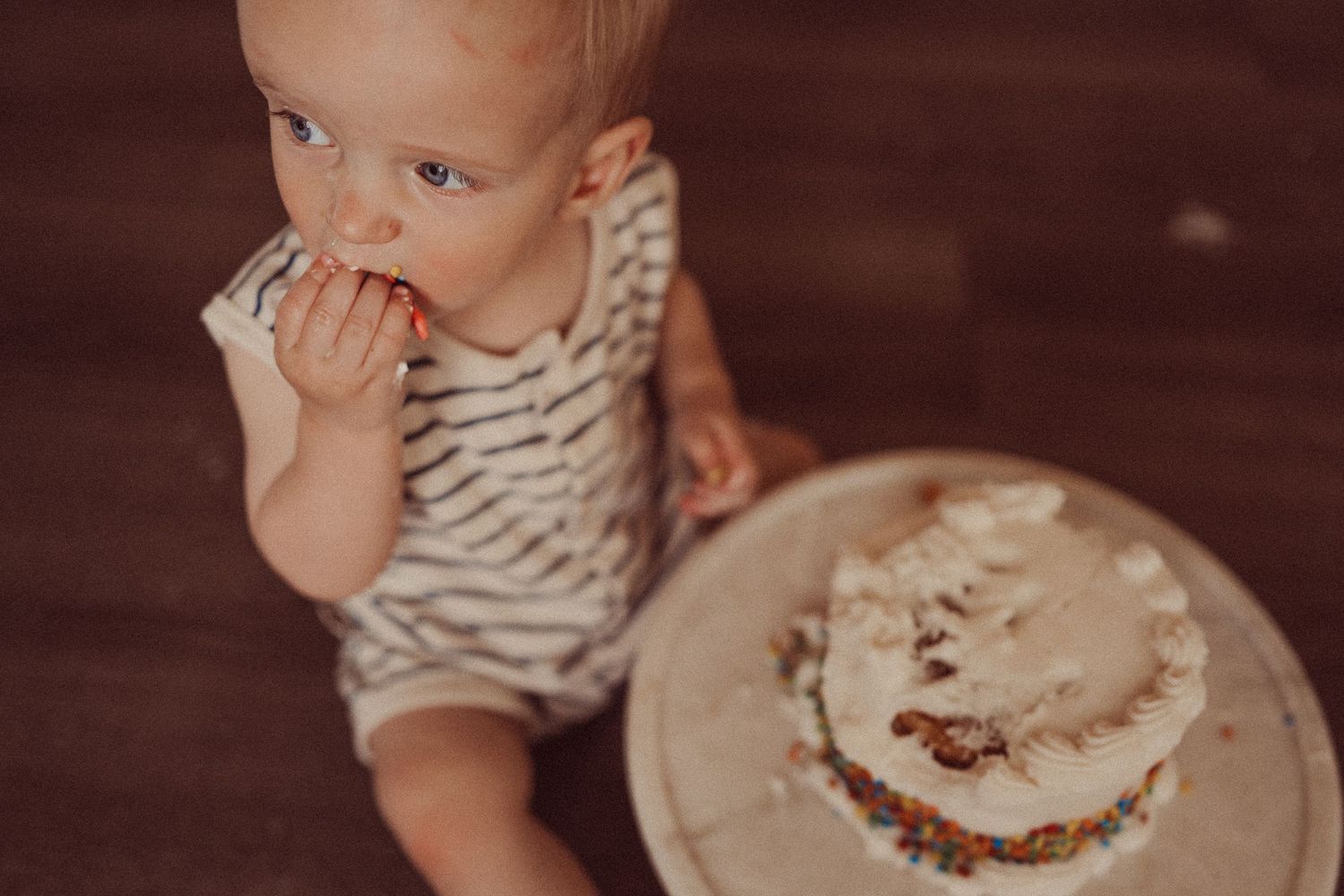 Close-up of toddler eating cake during first birthday photo shoot on wooden floor.