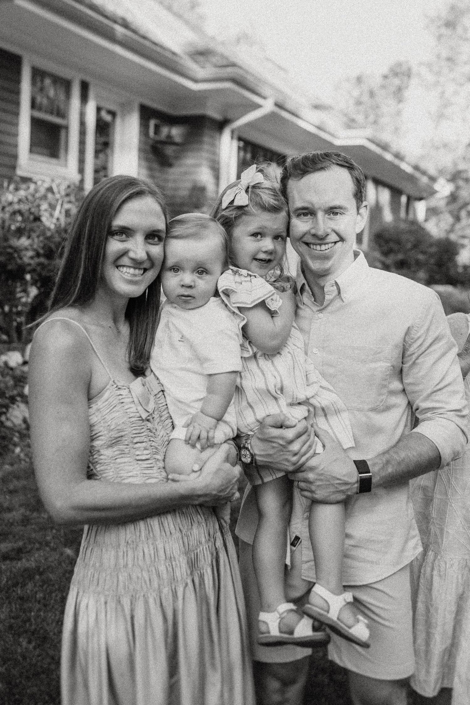 Black and white portrait of a young family with small children outside their home.