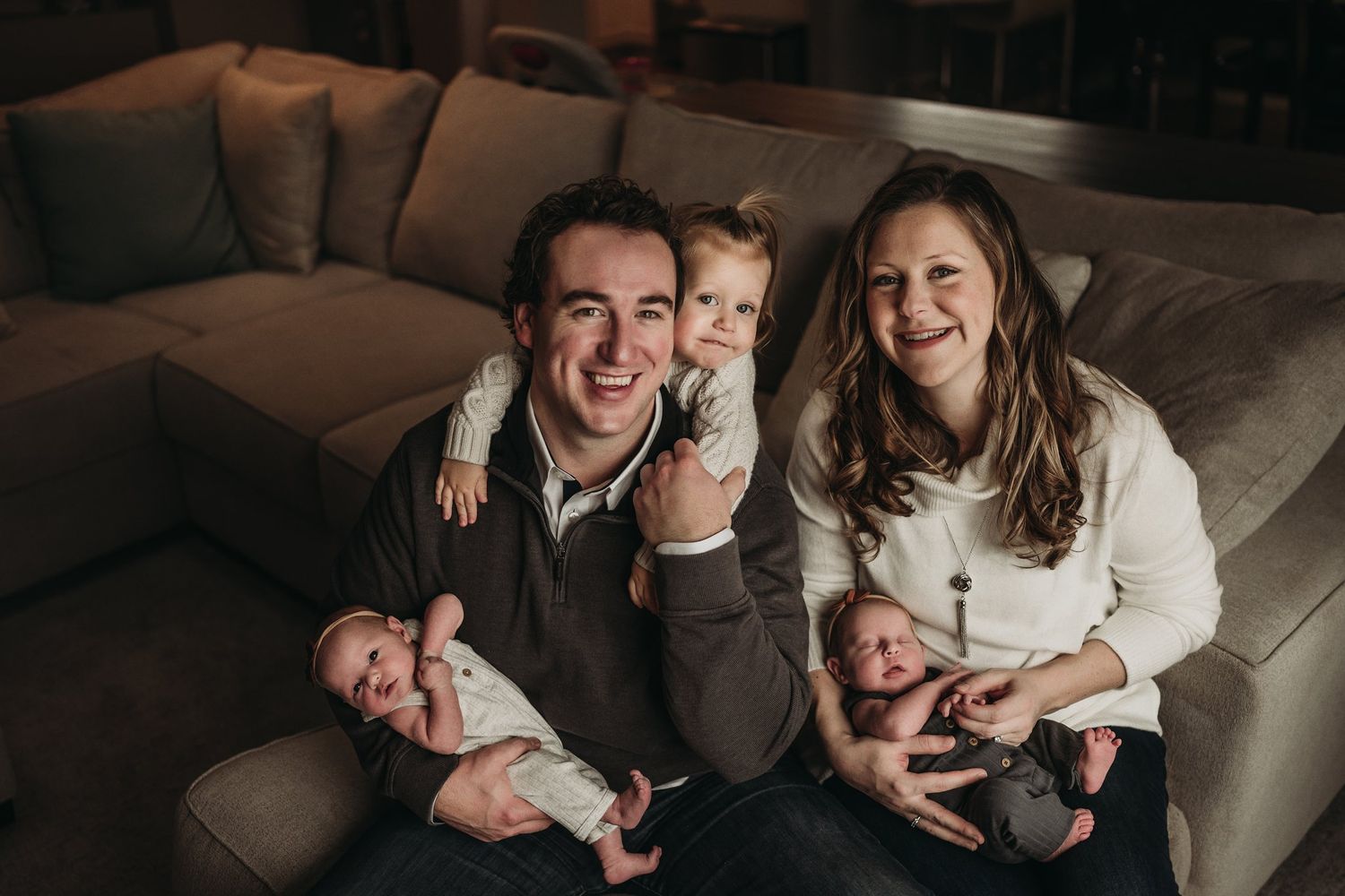 Candid family portrait on grey couch with twins and toddler.
