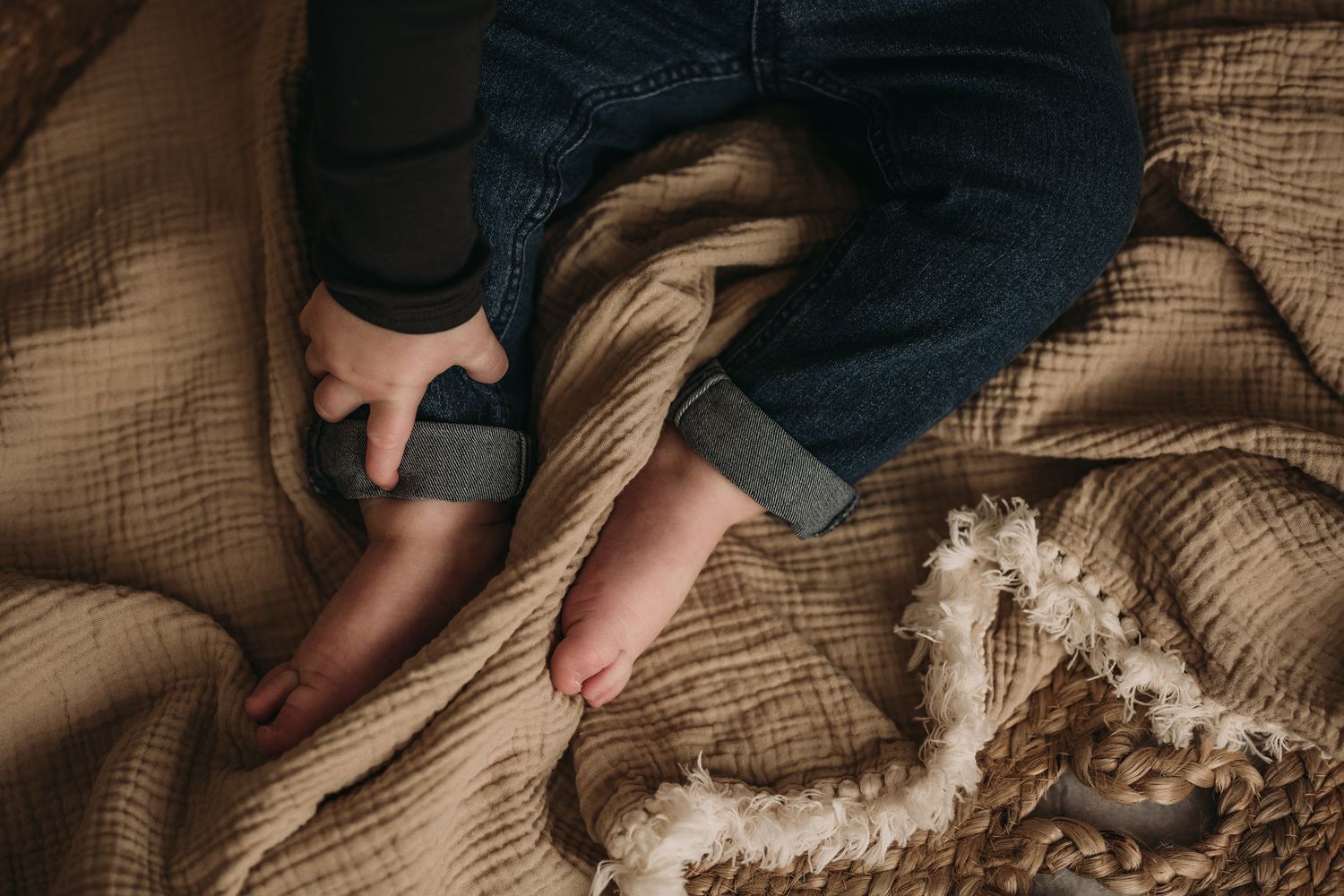 Detail shot of small bare feet on beige textured fabric with rope accents.