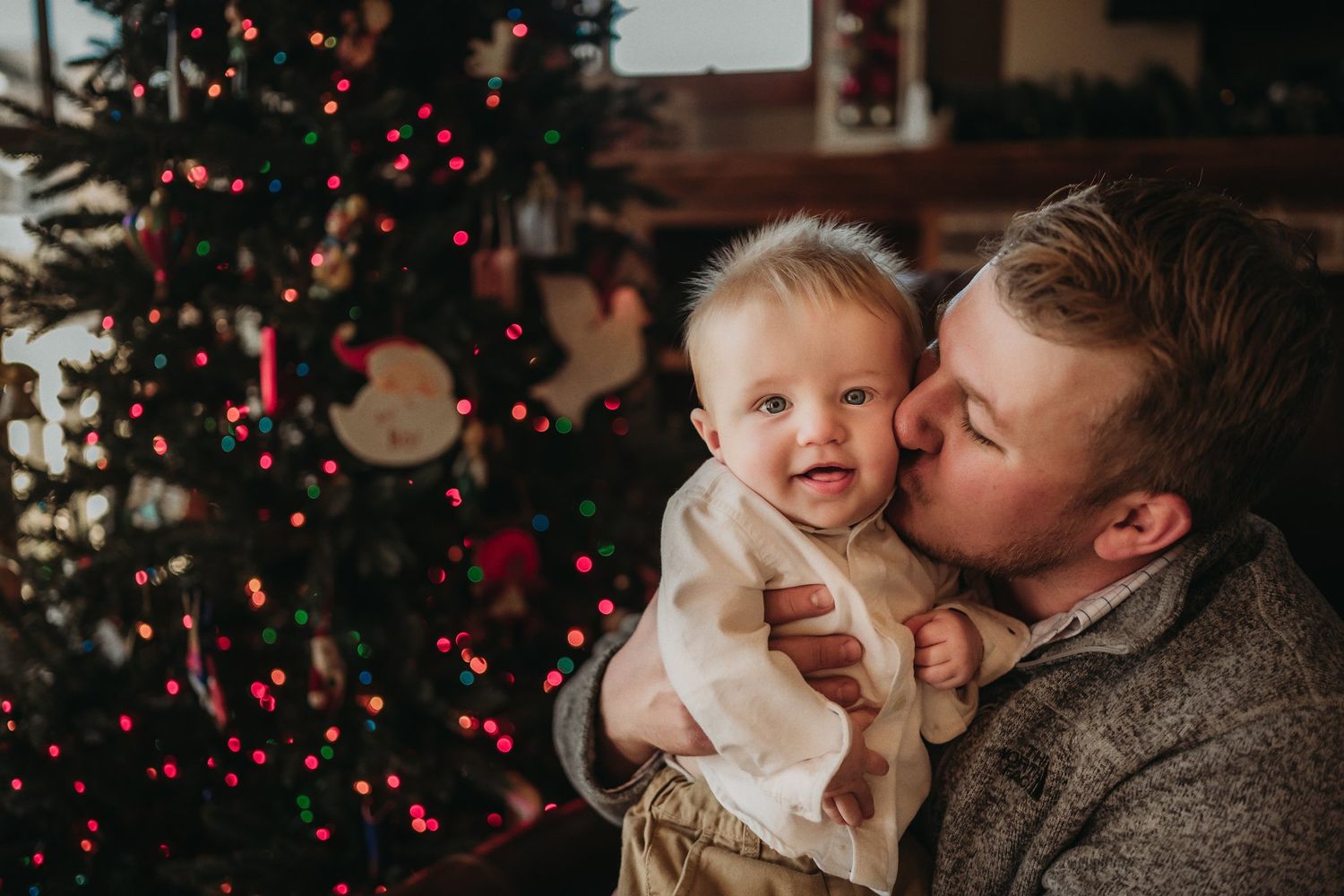 Intimate holiday portrait near Christmas tree with red lights and decorations.