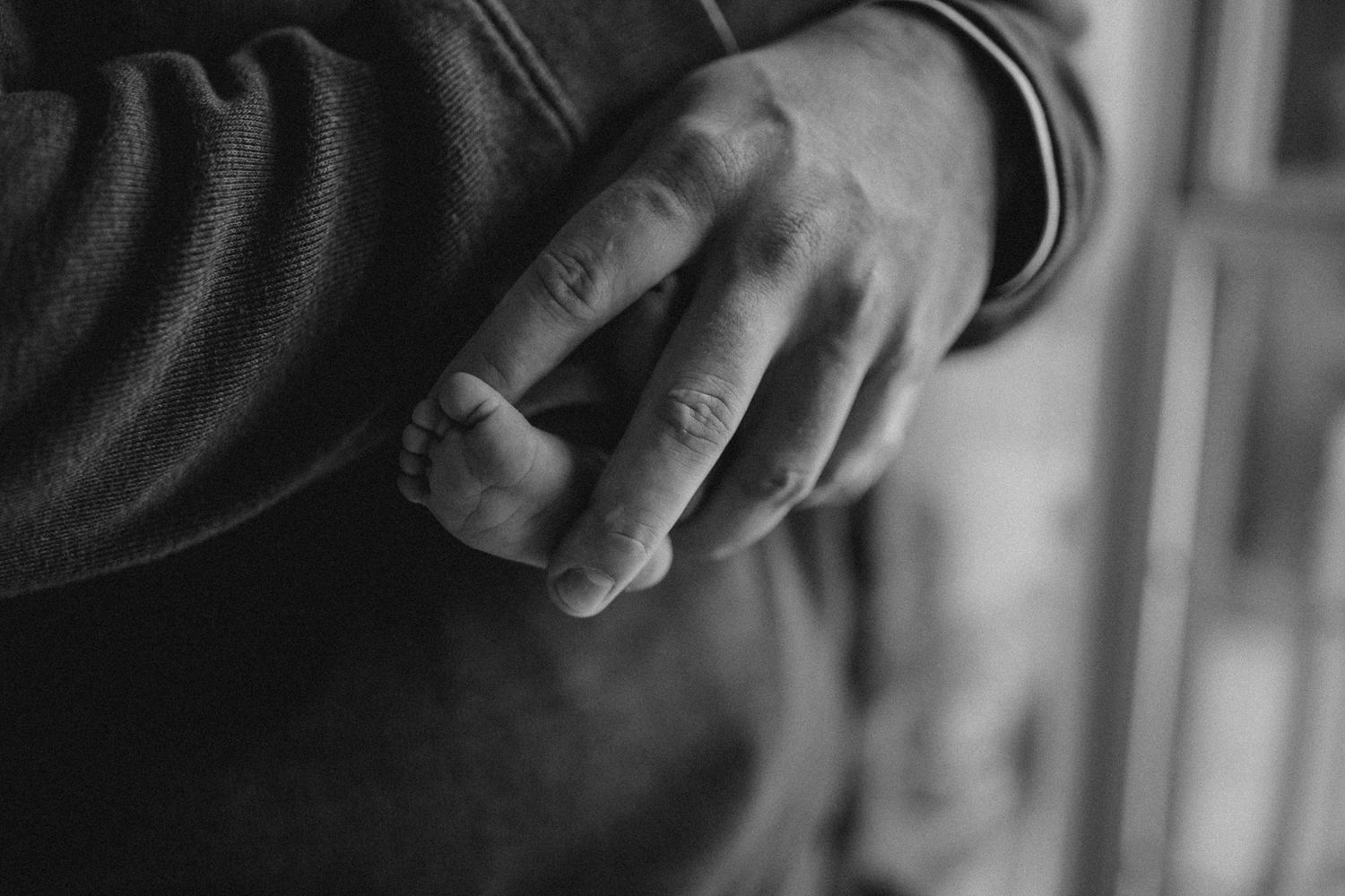 Close-up black and white detail shot of hands resting gently against dark fabric.