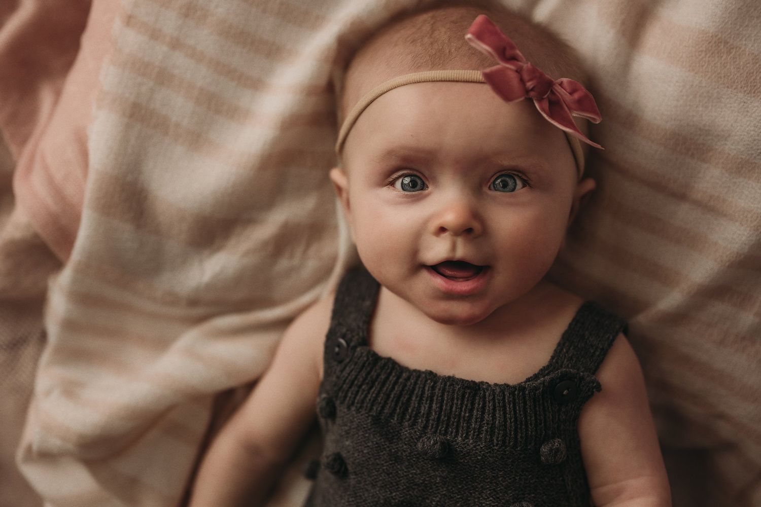Close up portrait of baby in dark romper against soft pink background.