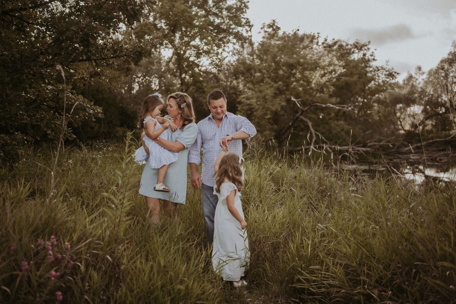 A family dressed in light colors poses together in a sunlit meadow during golden hour.