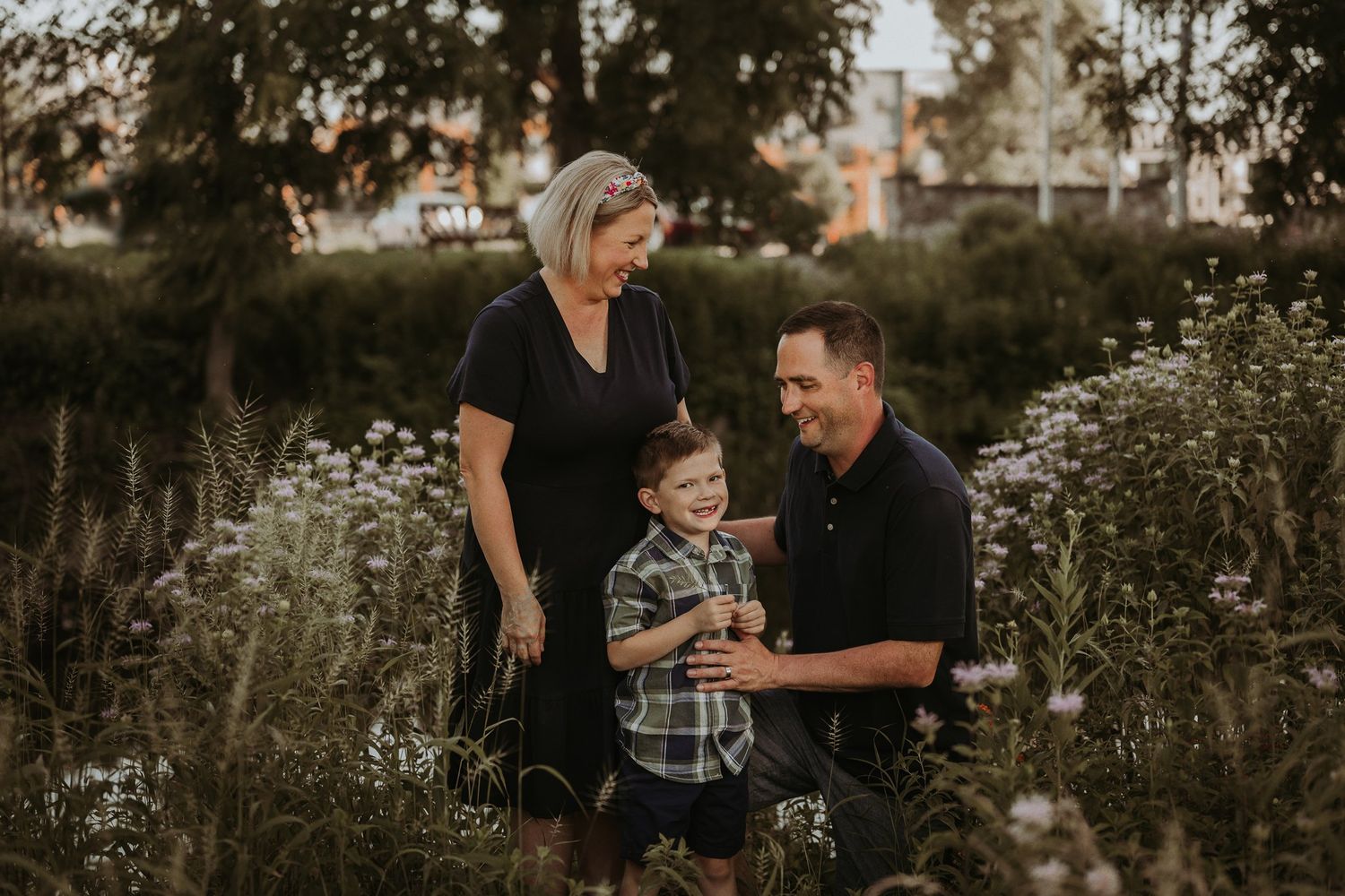 Family shares intimate moment together while kneeling in wildflower meadow at sunset.