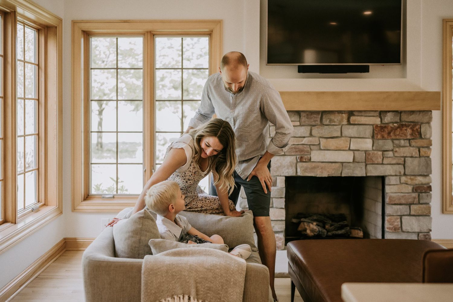 Family enjoying quality time together in their living room with stone fireplace and large windows.