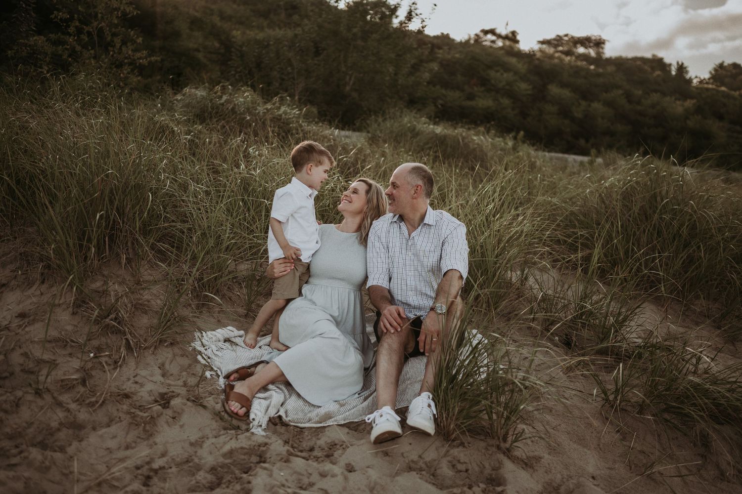 Family shares joyful moment together while sitting on sandy hill.