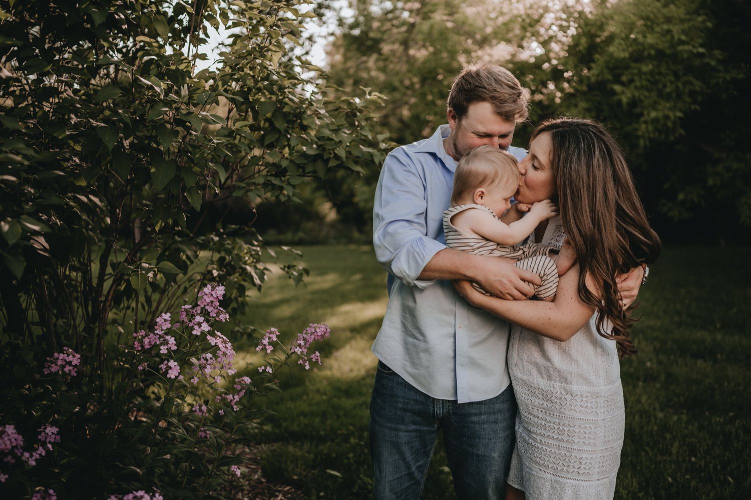 A tender outdoor family moment captured in a garden with blooming flowers at sunset.