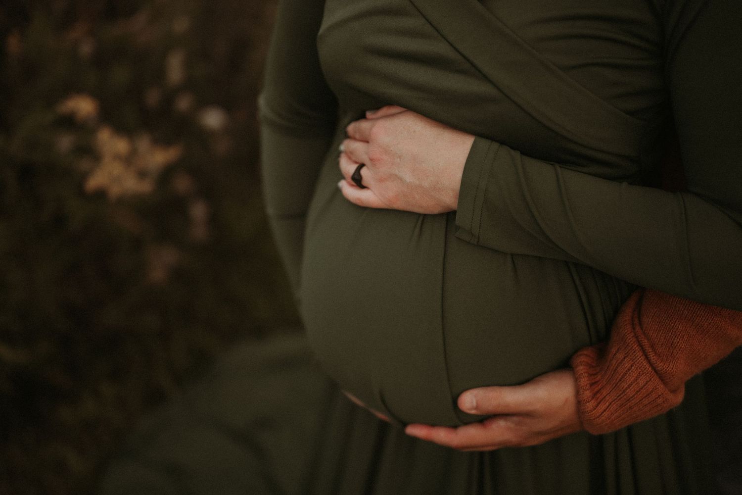 Hands tenderly cradle a pregnant belly draped in dark green fabric.