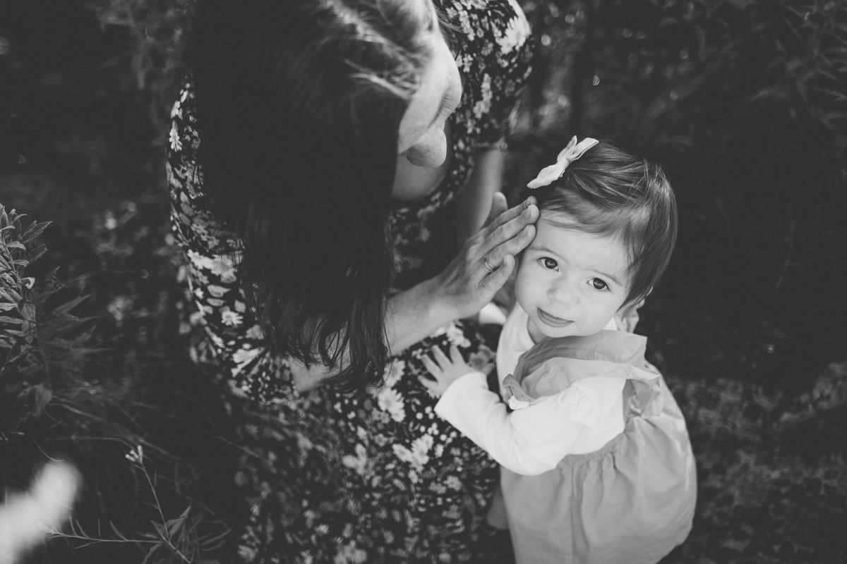 A black and white portrait capturing a sweet moment between parent and child in nature.