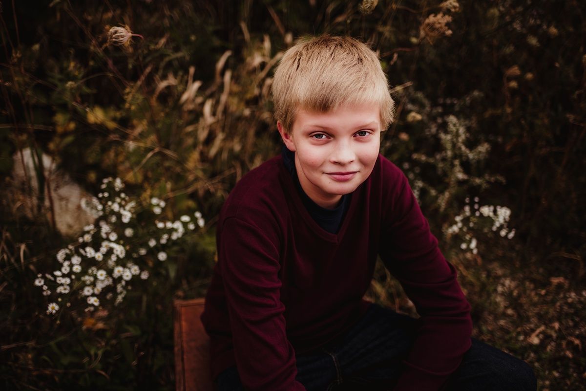 A portrait of a young person wearing a burgundy sweater sitting outdoors among wildflowers.