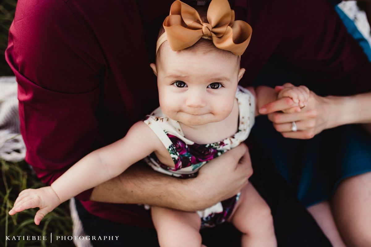 Close-up portrait of a baby wearing a brown bow and floral outfit.