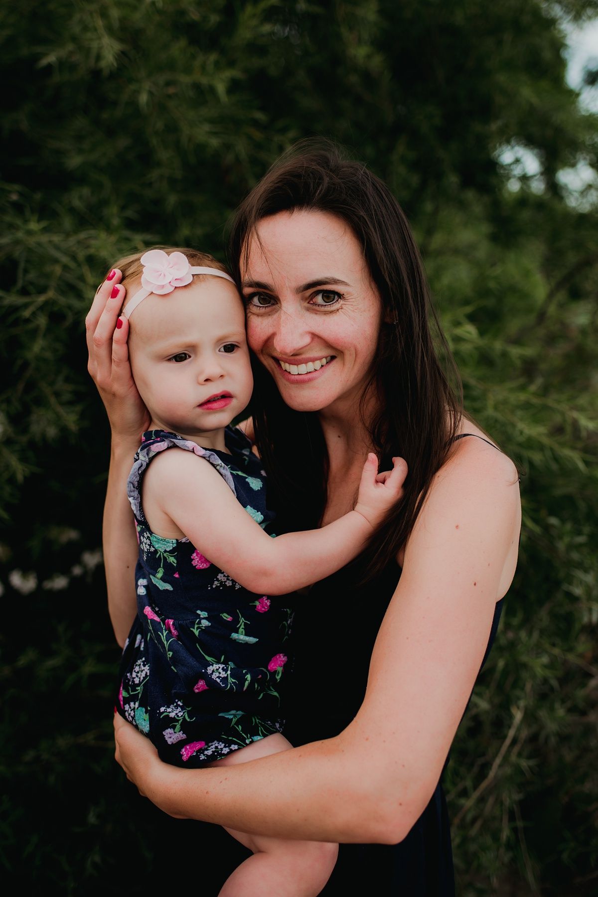 A sweet outdoor portrait of parent and child embracing among green foliage.