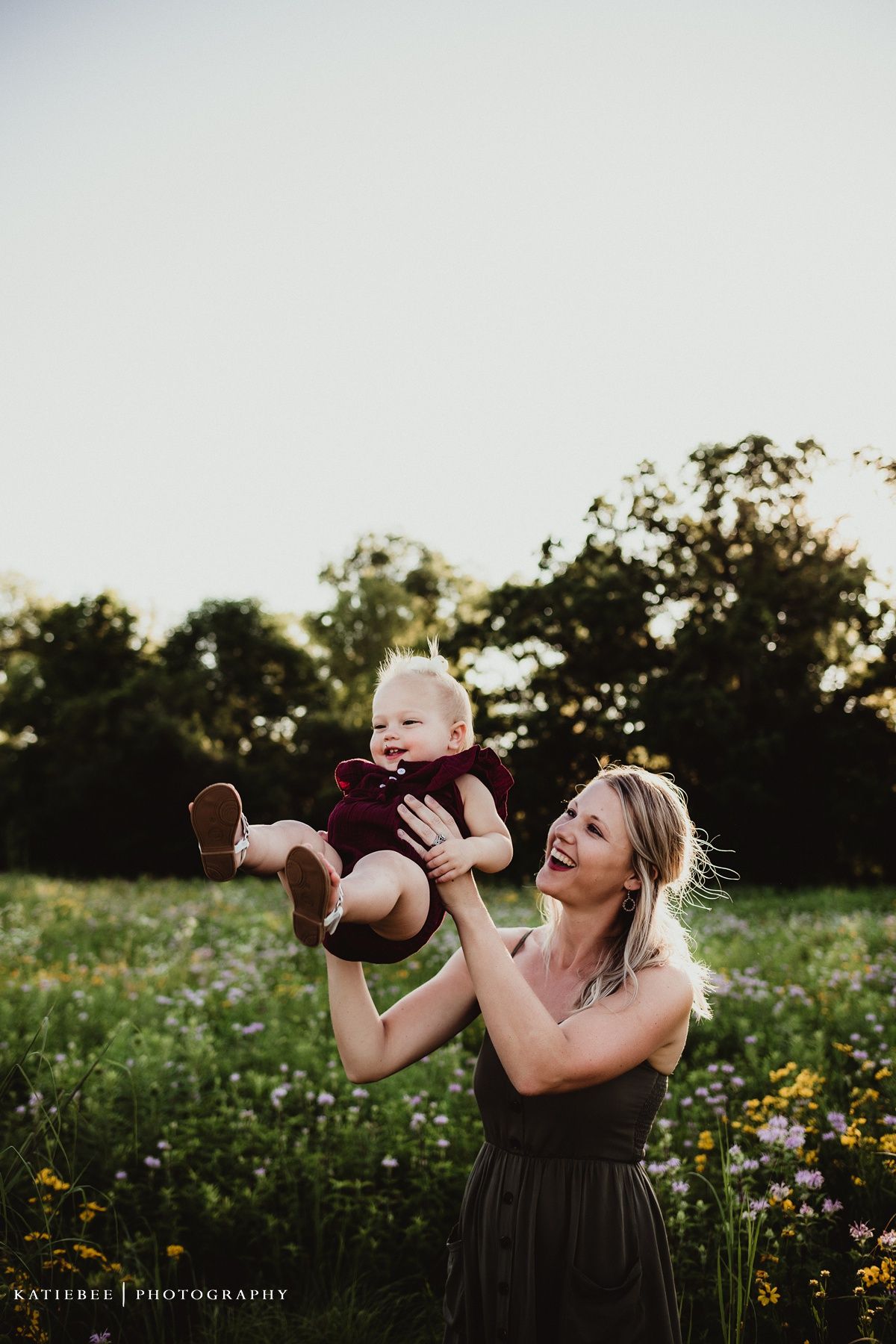 Playful outdoor portrait with baby being lifted in golden evening light.