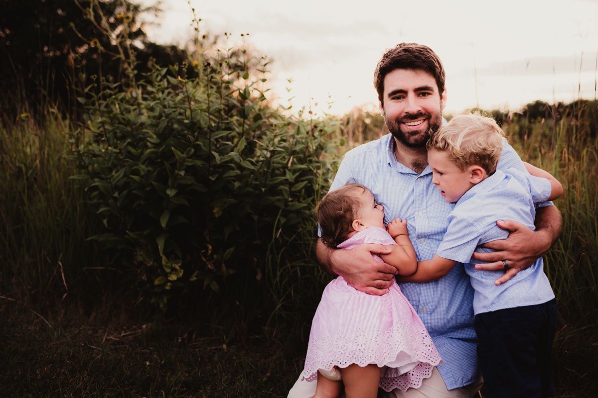 Warm family embrace captured in golden evening light among wild grasses.