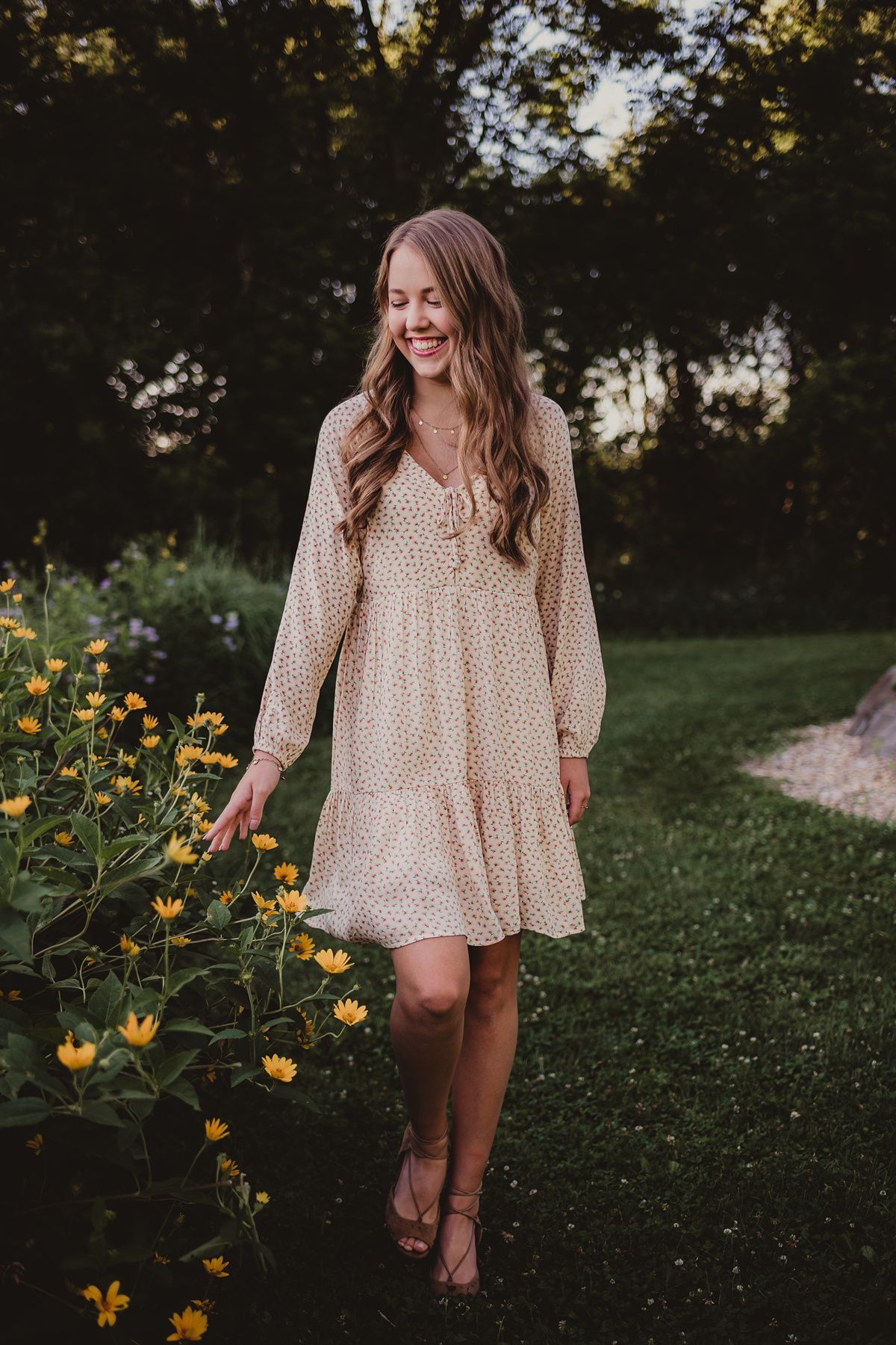 Candid garden photo walking barefoot past yellow flowers in cream summer dress.