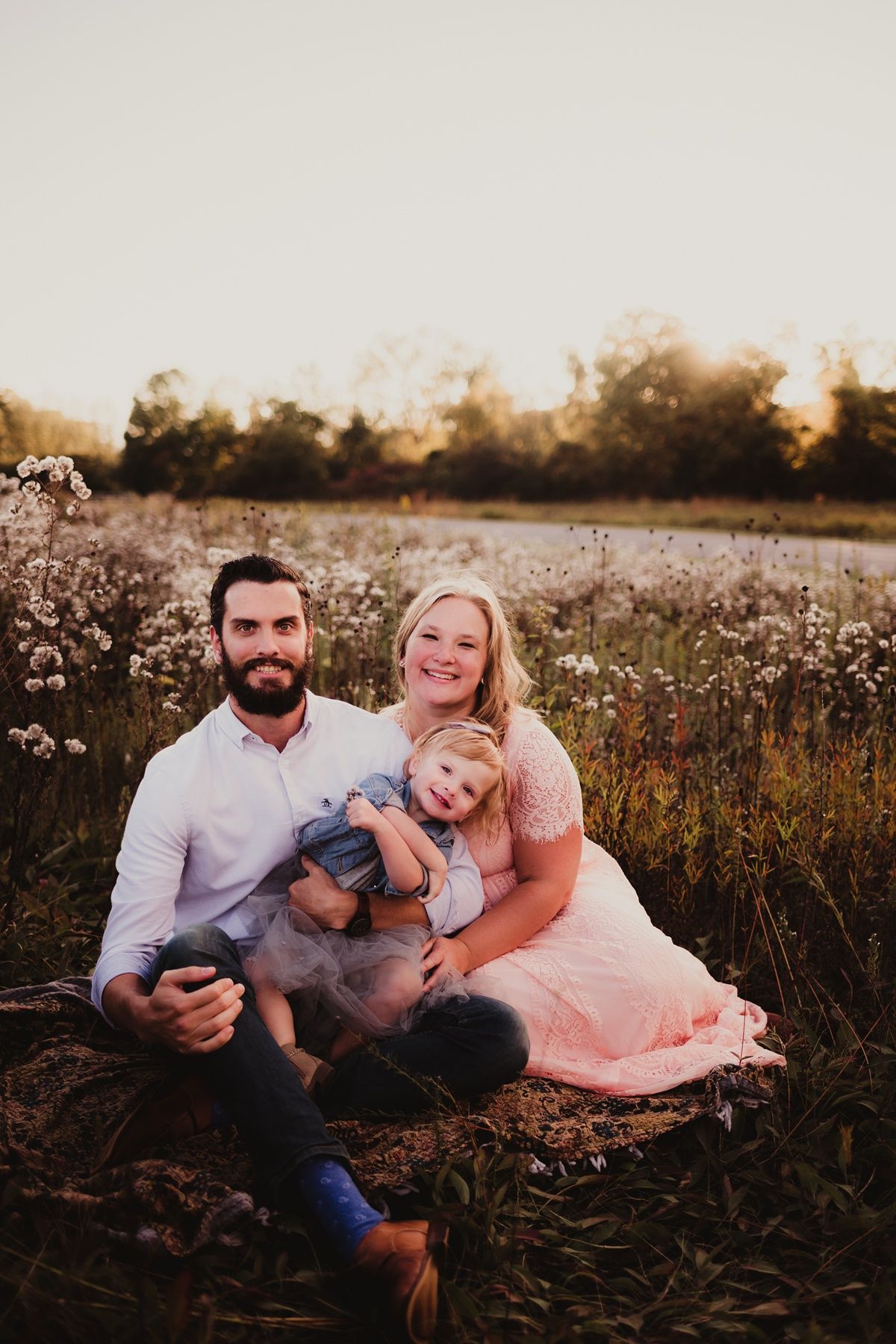 Family portrait in a wildflower meadow at sunset with pink dress and white shirt.