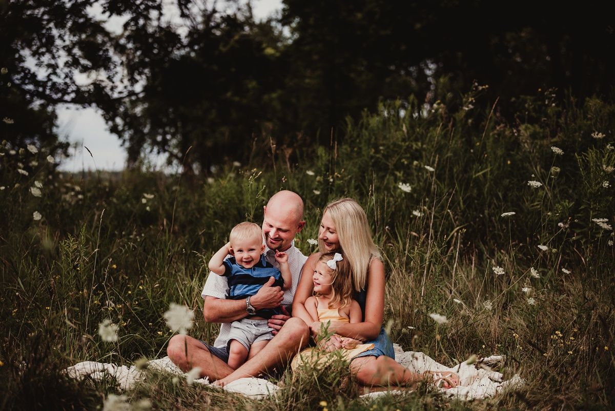 Family sitting together on a blanket in a field of wildflowers during sunset.