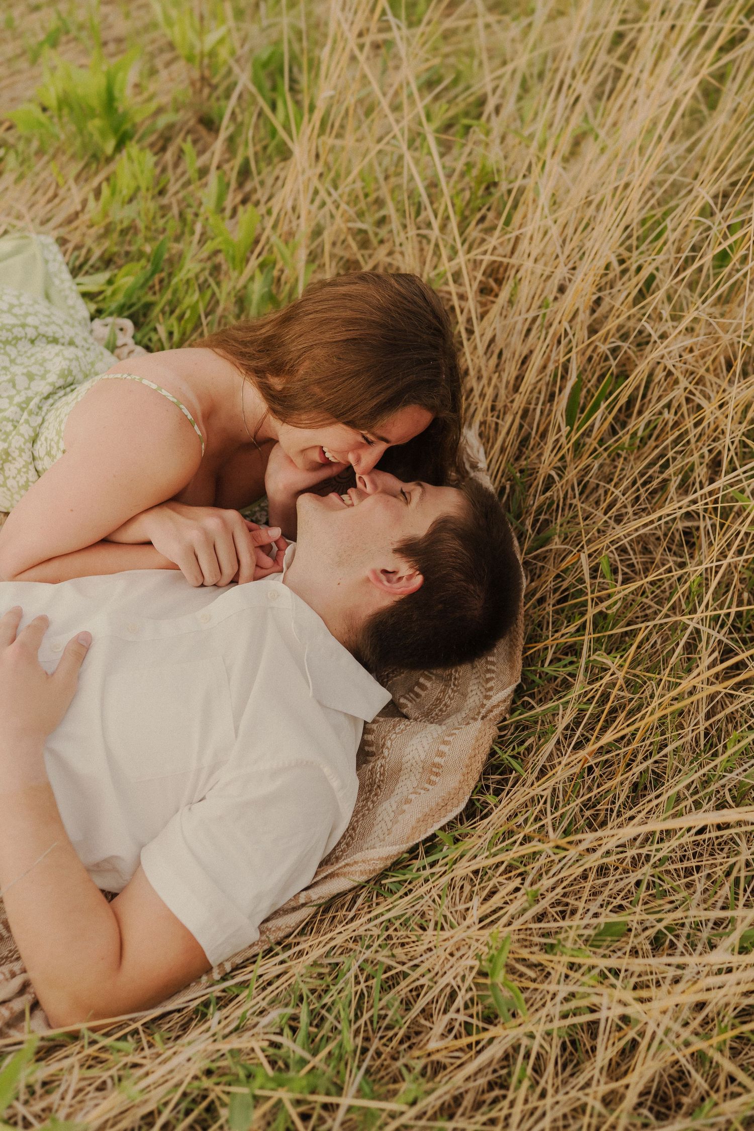 Romantic couple sharing an intimate moment while lying in tall grass during a warm afternoon.