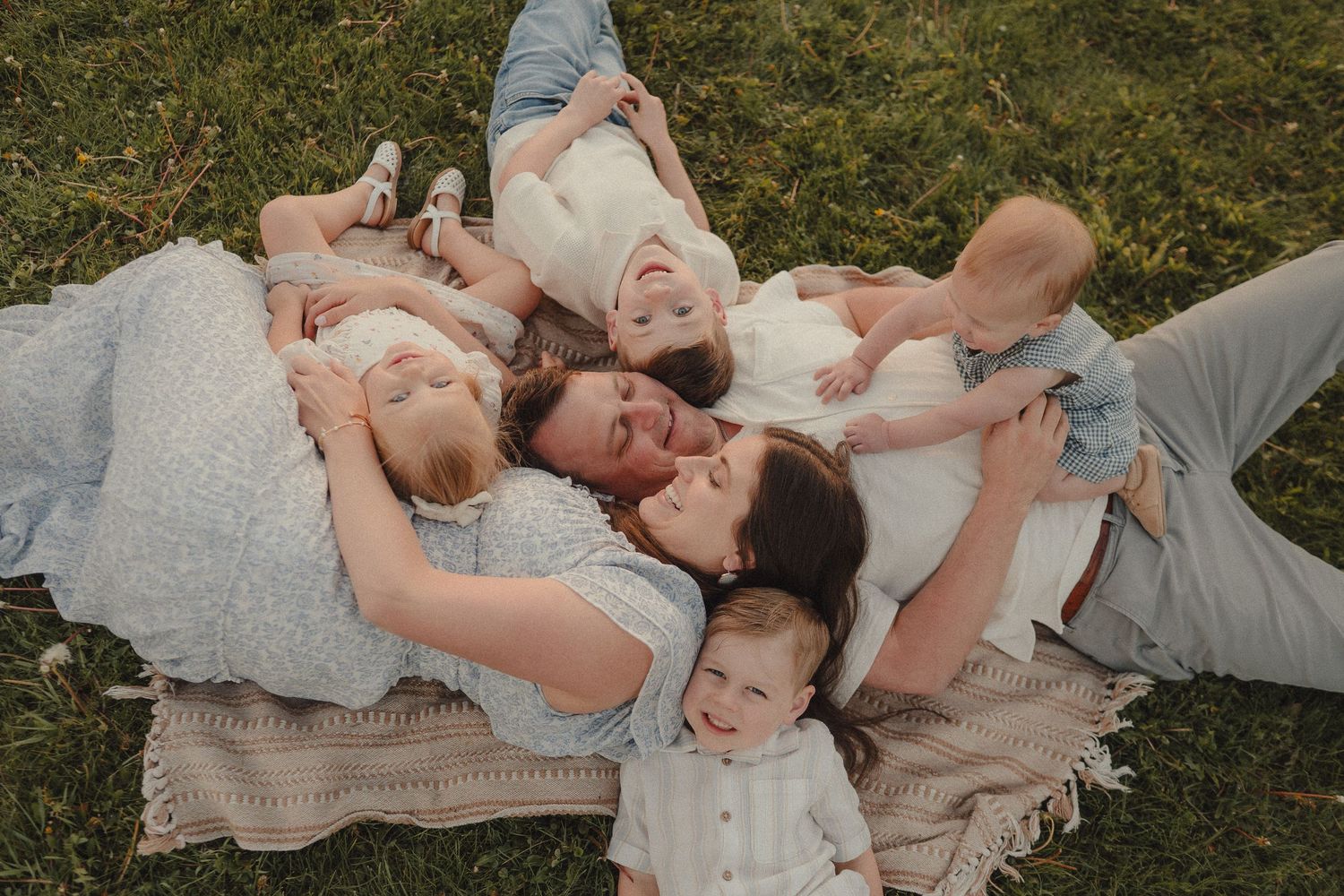 Aerial view of a family lying on a blanket in the grass, cuddling and kissing their children.