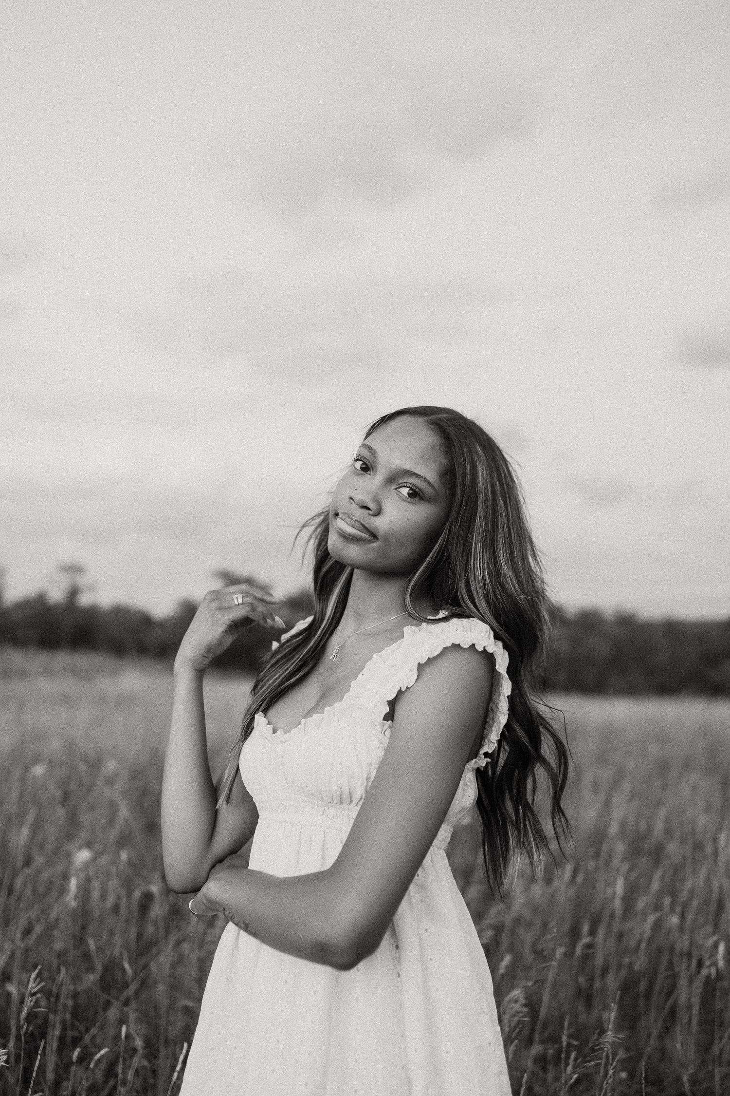 Black and white portrait of a young woman in a white dress standing gracefully in an open field.